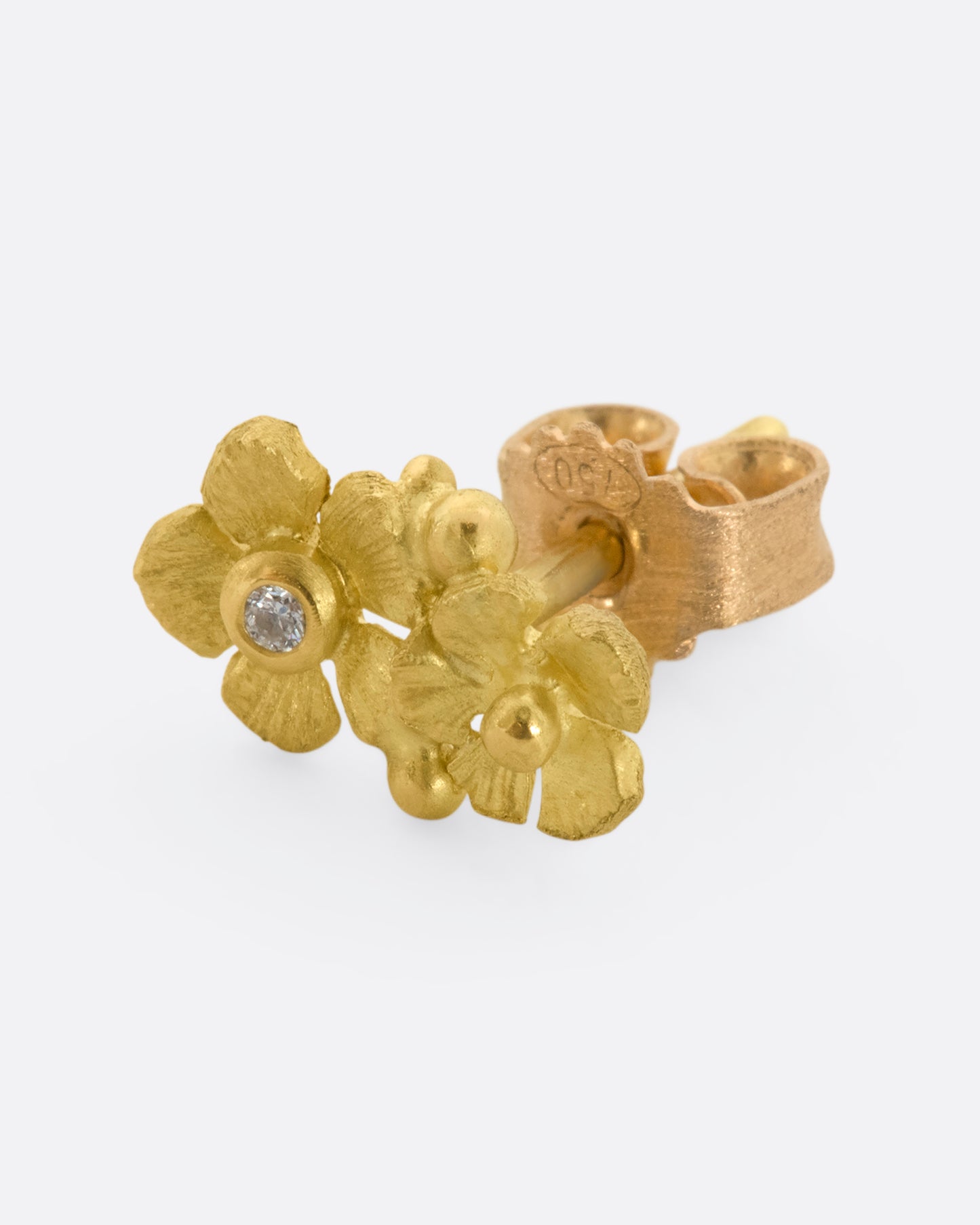 A yellow gold earring with two flowers, one with a diamond at the center. View from the side.