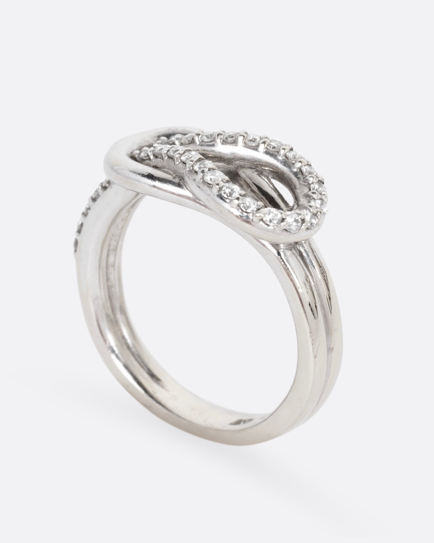 A white gold ring with a diamond studded infinity knot, shown from the side standing up.