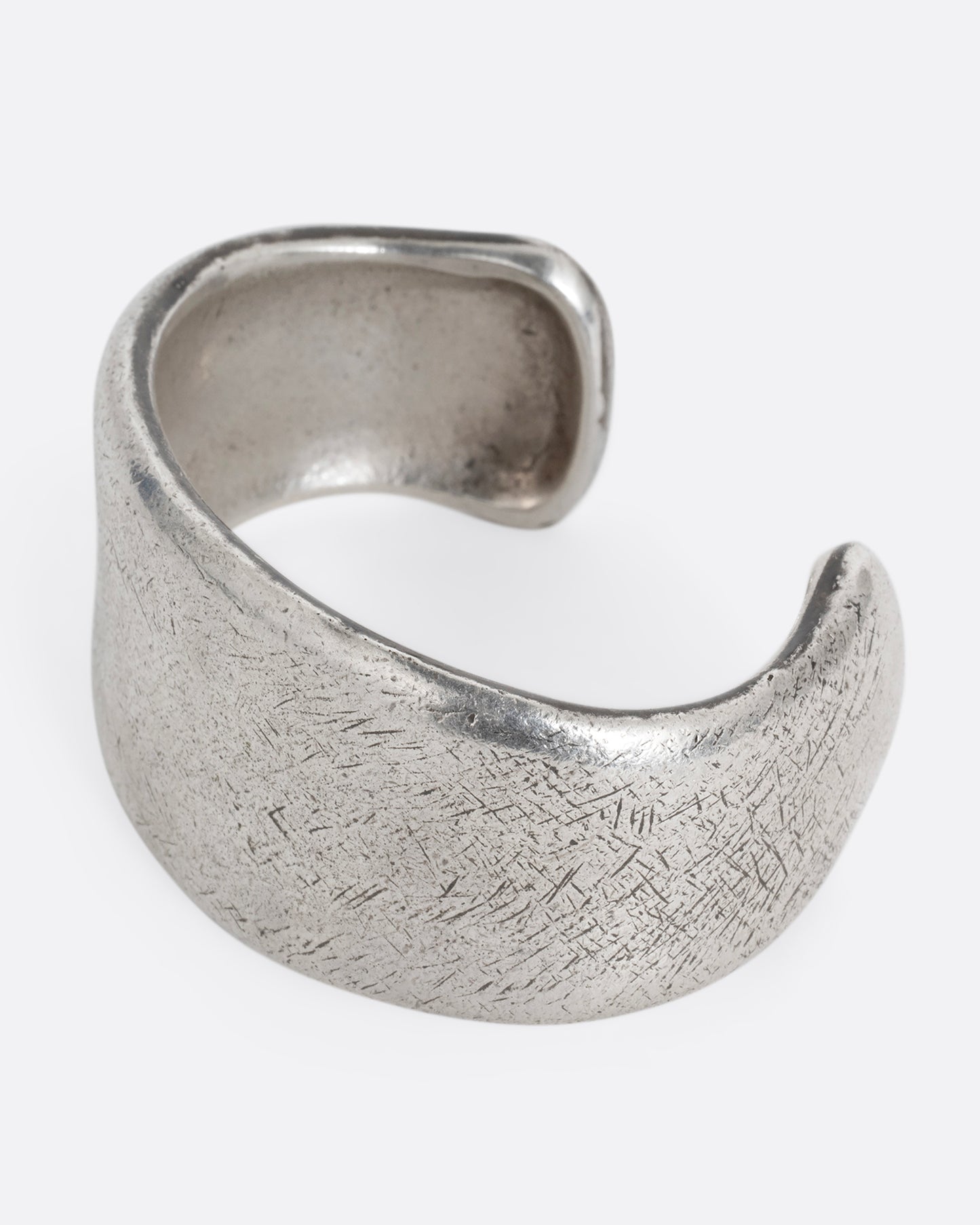 A silver cuff bracelet with a patinated finish and smooth edges. Shown from the side.