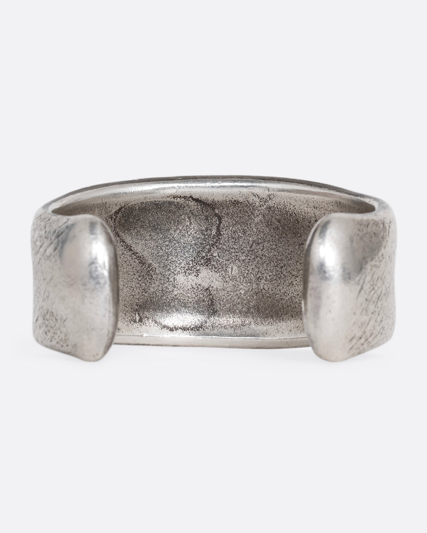 A silver cuff bracelet with a patinated finish and smooth edges. Shown from the back.