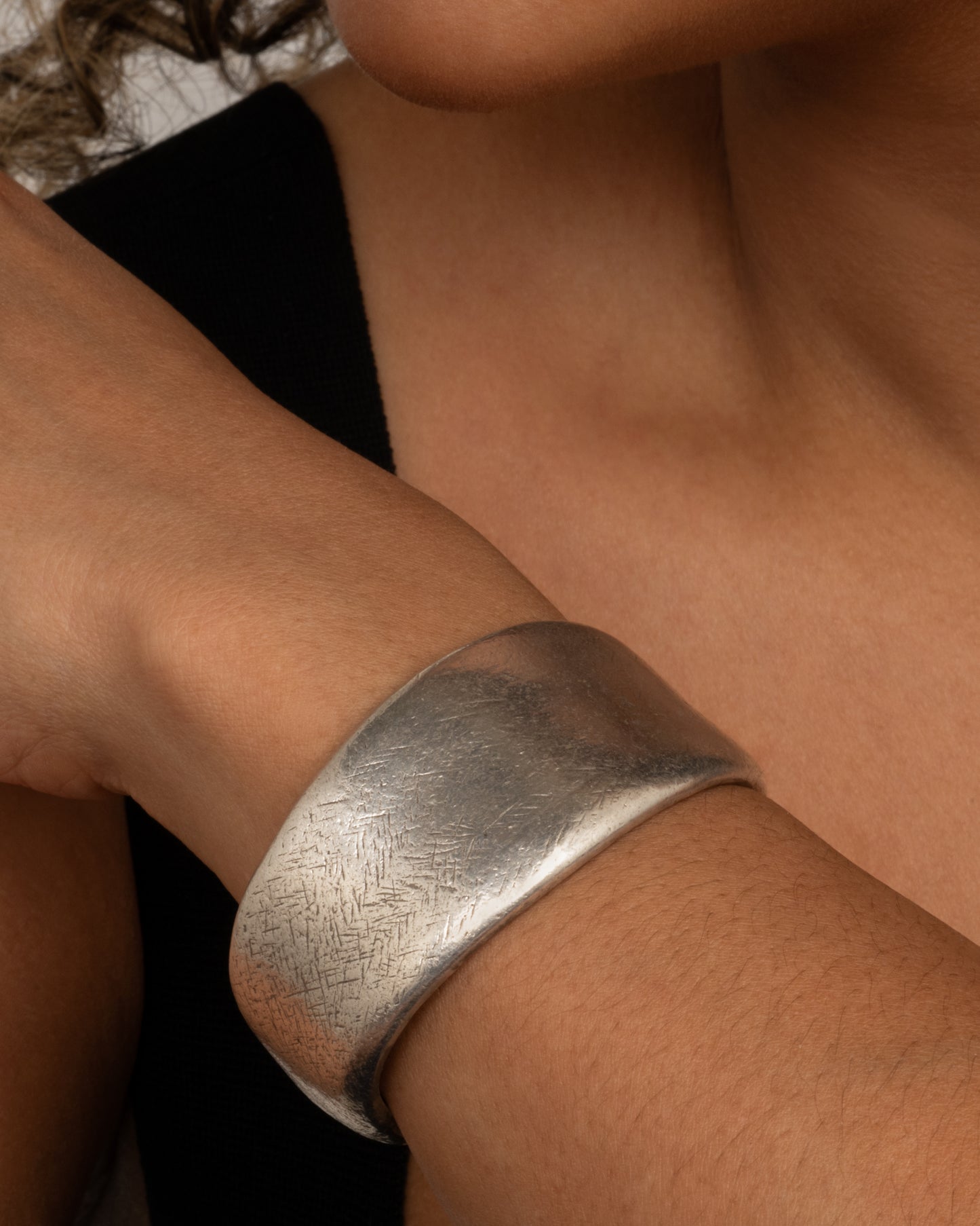 A silver cuff bracelet with a patinated finish and smooth edges. Shown from the front on a person.