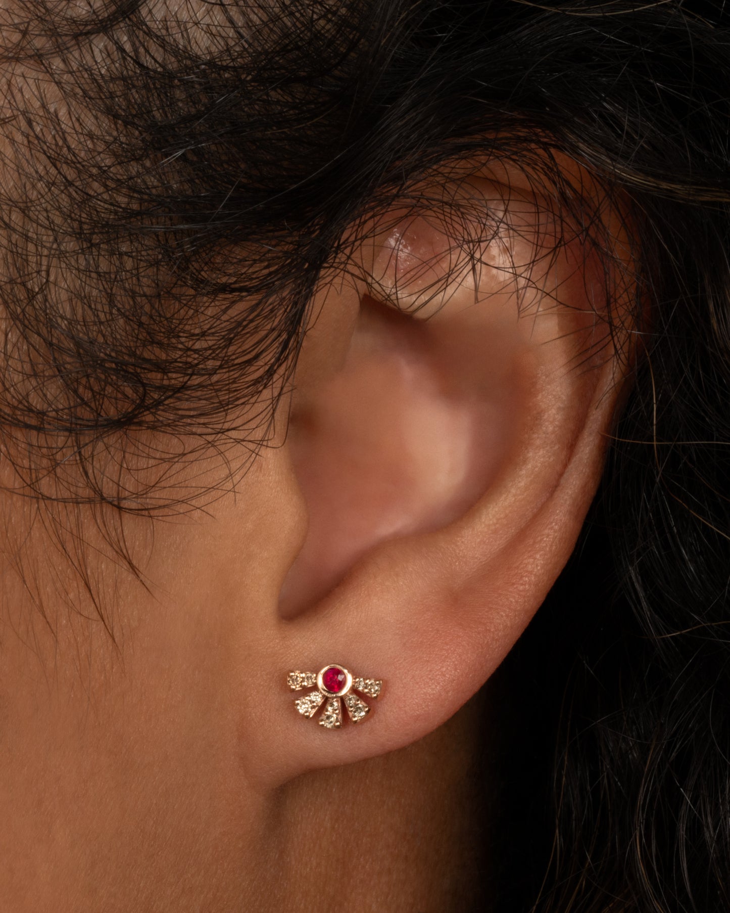 A single rose gold earring with a ruby in the middle and five black diamond pave bars extending from the ruby. Shown worn in an ear.
