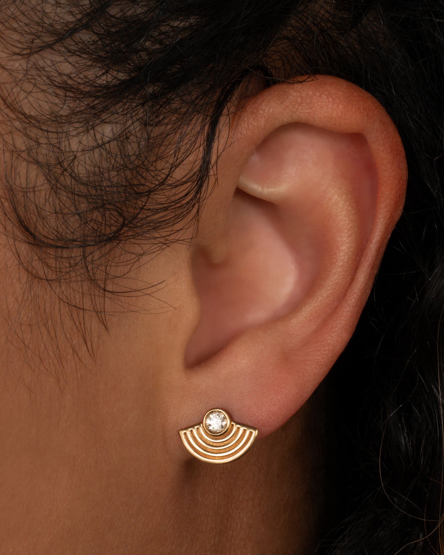 A yellow gold stud earring in a rainbow shape with a diamond at the top center. Shown from the front on a person.