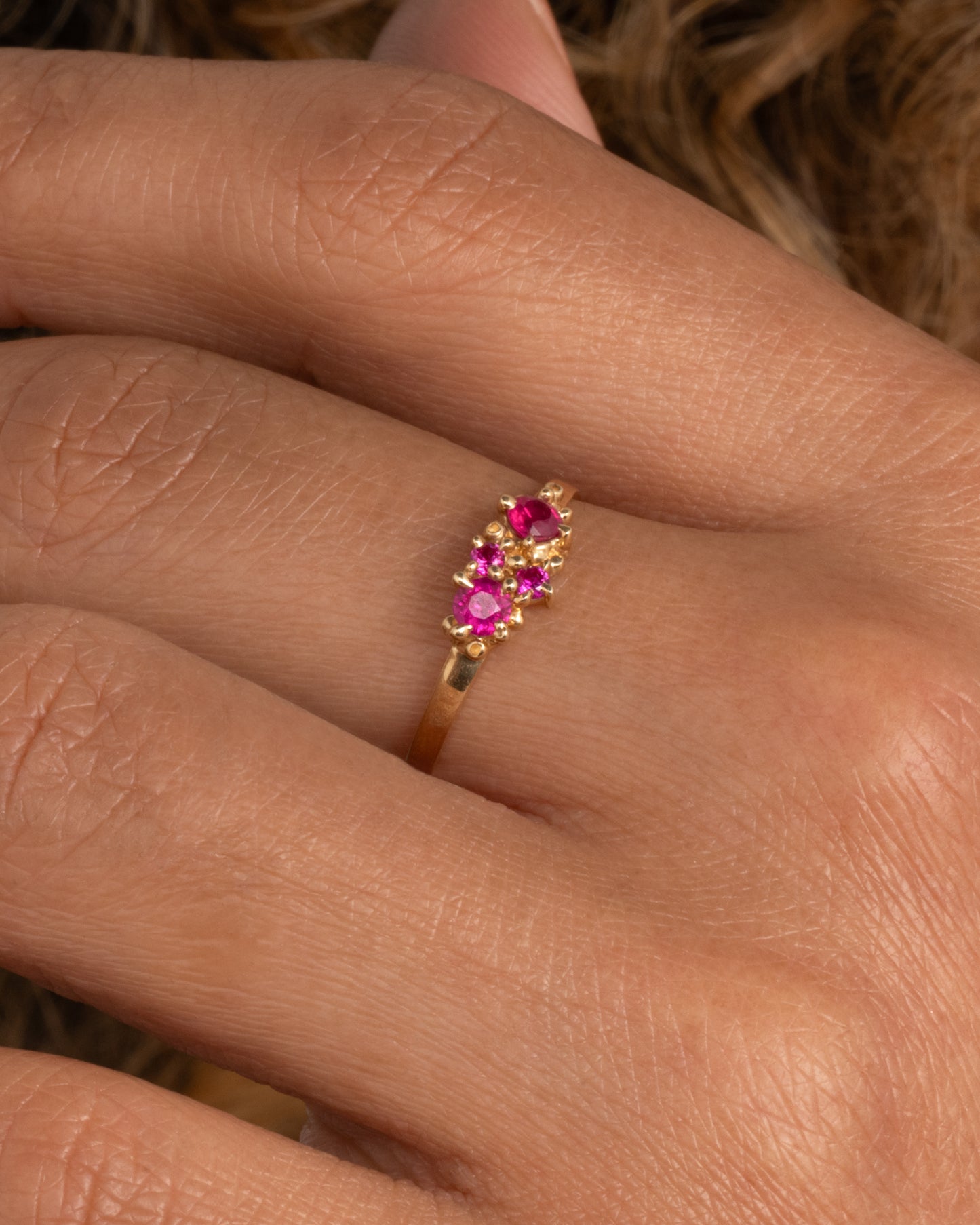 A yellow gold ring with a cluster of four rubies. Shown worn on hand.