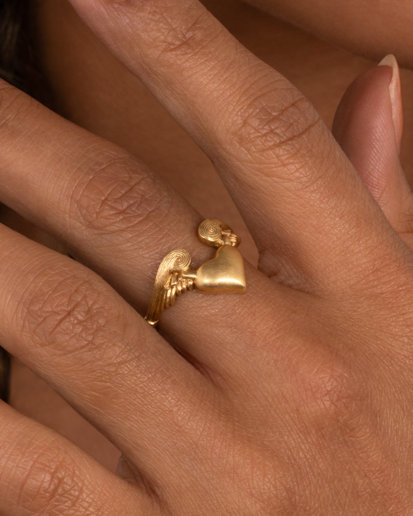 A yellow gold ring with a heart with wings on it. Shown worn on hand.