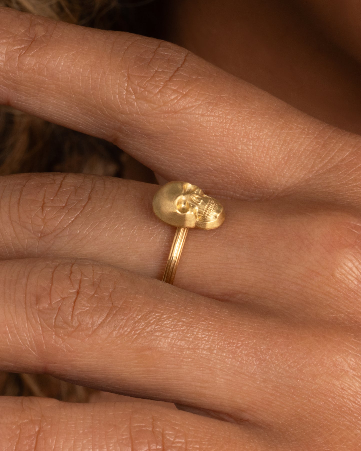 On hand view of yellow gold ring with a sculpted skull charm on a round fluted band.