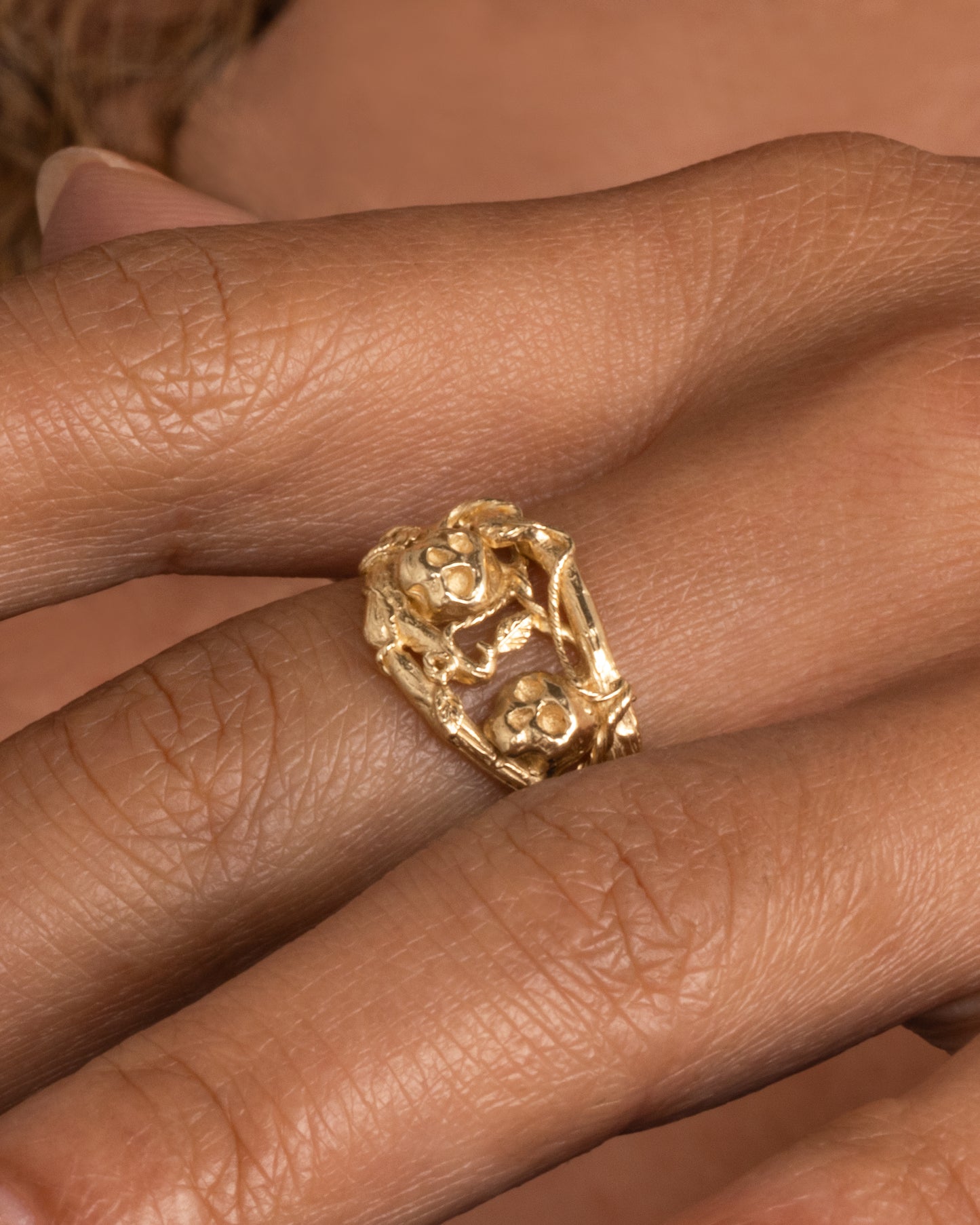 A yellow gold momento mori ring with organic branch and vine motif, featuring two skulls. Shown worn on hand.
