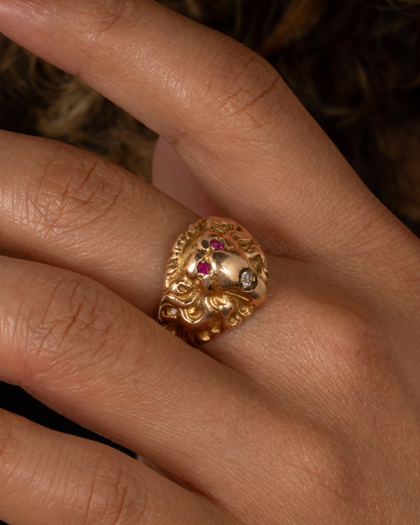 A yellow gold lion ring with ruby eyes and a single diamond in its mouth. Shown from the front on a person.