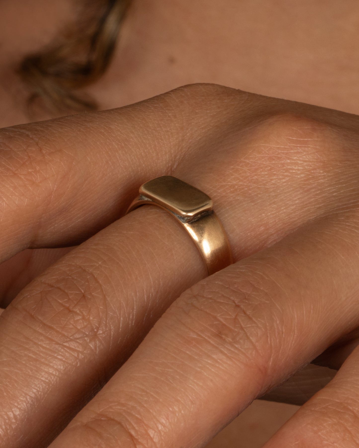 A yellow gold signet ring with a rectangular face. Shown from the side on a person.