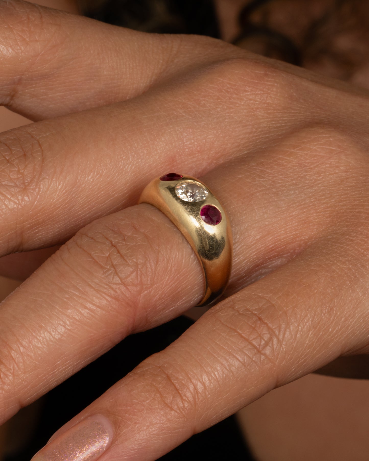 A yellow gold dome ring with a central diamond flanked by two rubies. Shown from the side on a person.
