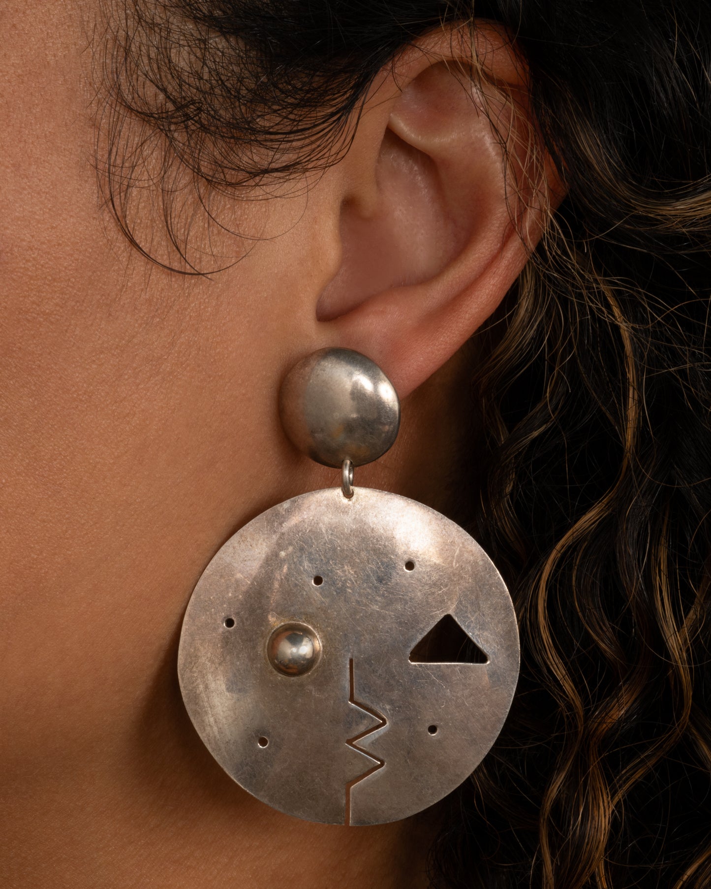 A round drop stud earring with geometric cutout face. Shown from the front on a person.