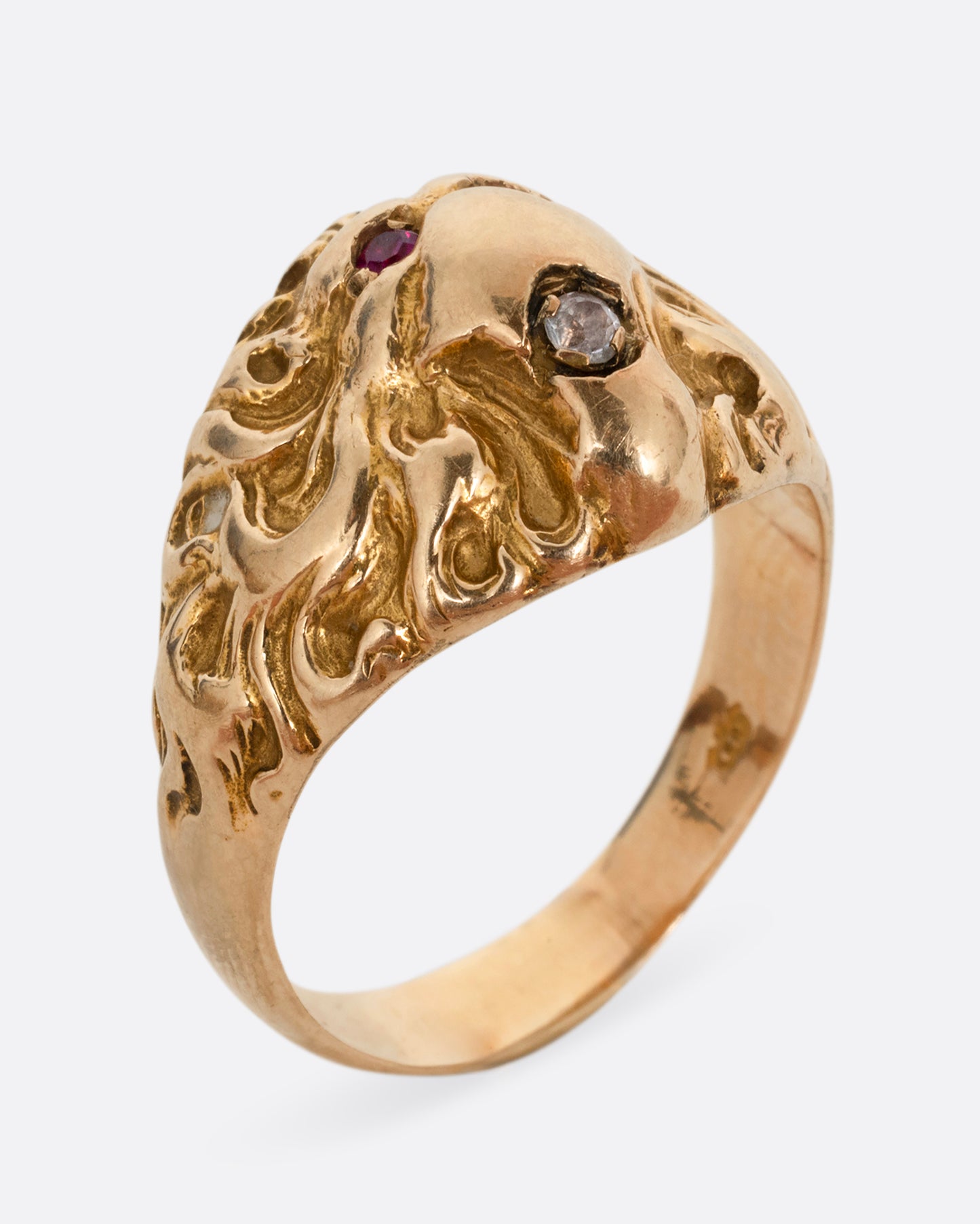 A yellow gold lion ring with ruby eyes and a single diamond in its mouth. Shown standing up from the side.