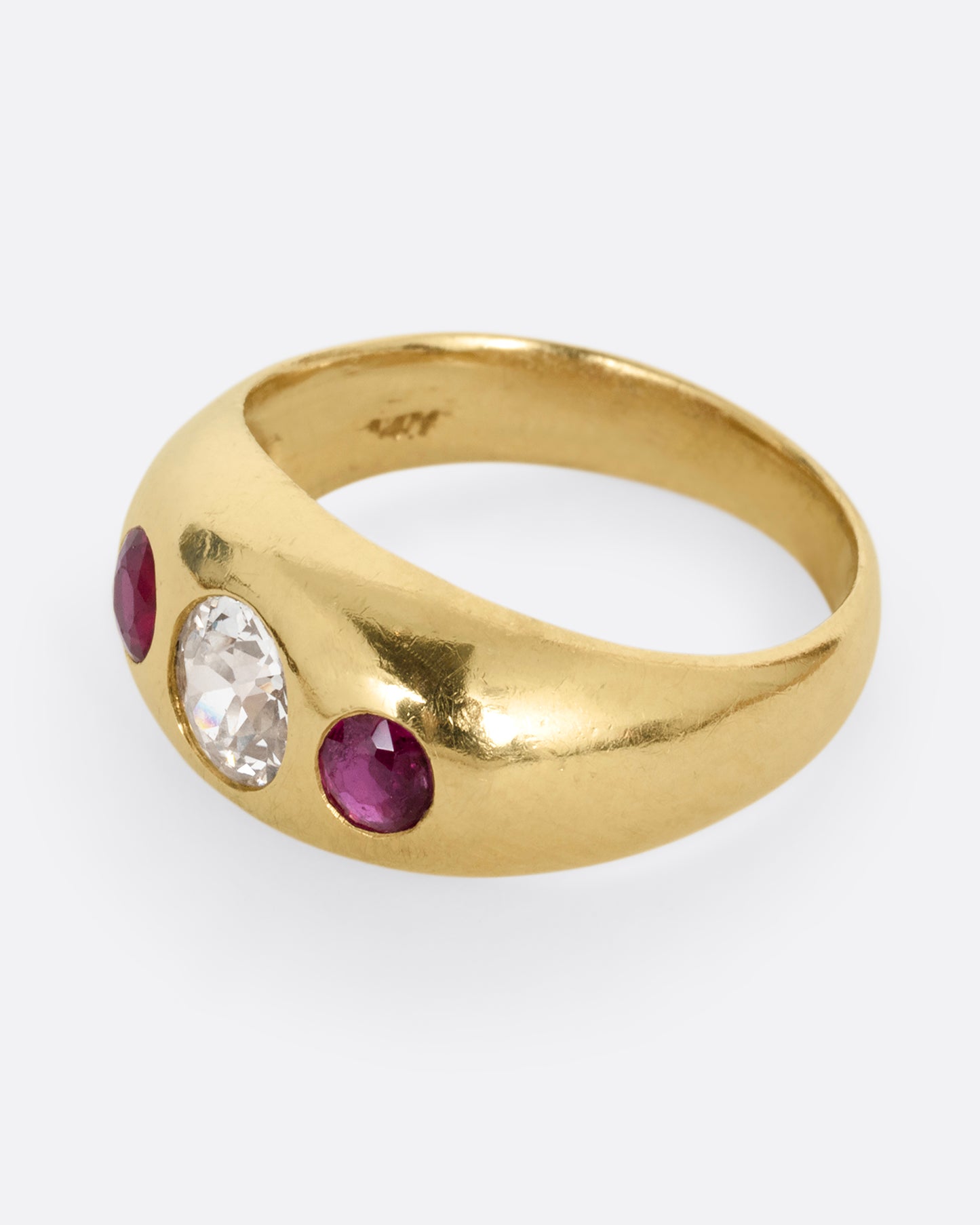 A yellow gold dome ring with a central diamond flanked by two rubies. Shown from the side.