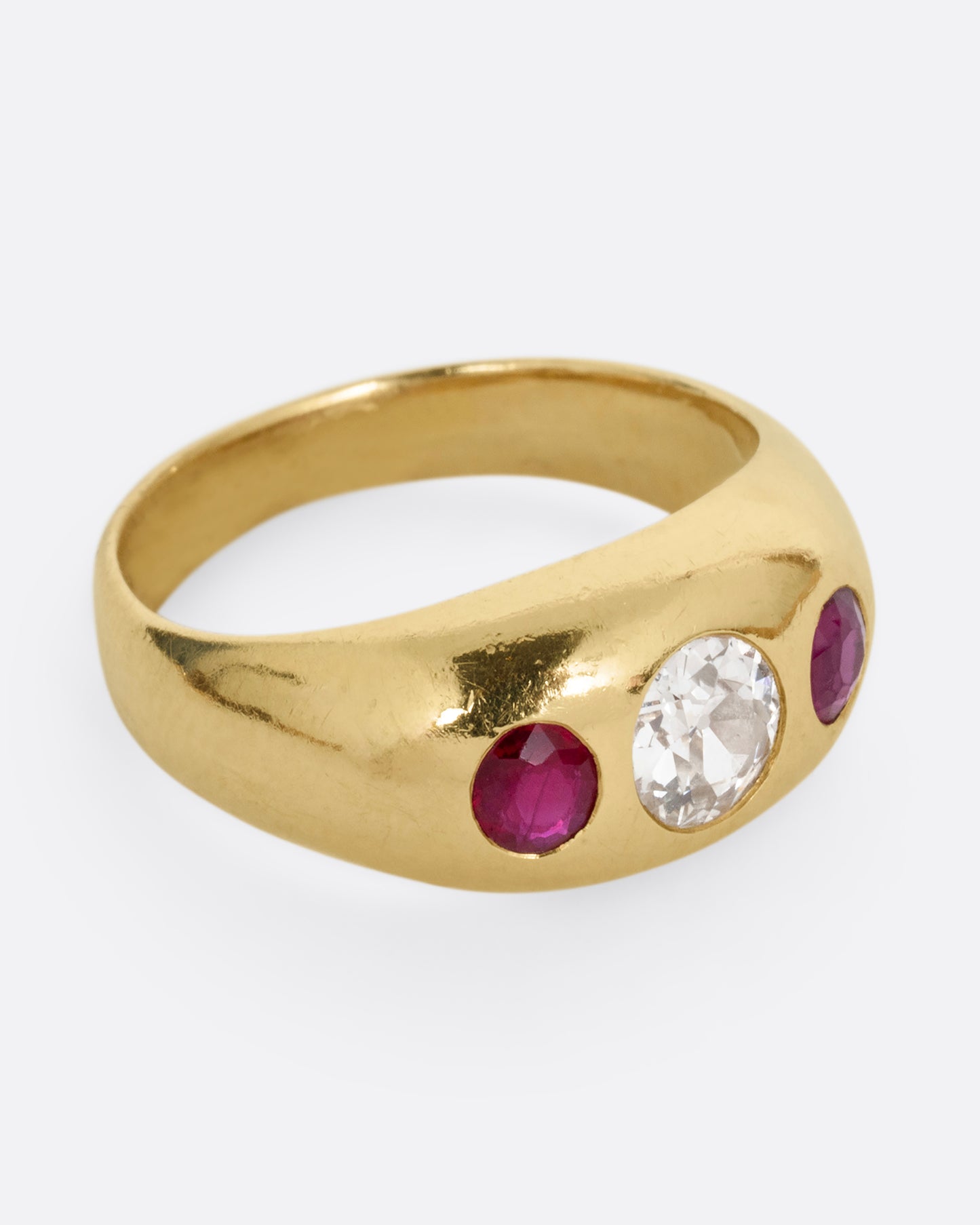 A yellow gold dome ring with a central diamond flanked by two rubies. Shown from the side.