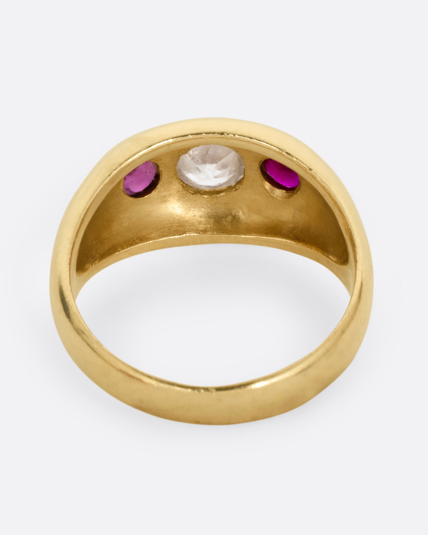A yellow gold dome ring with a central diamond flanked by two rubies. Shown from the back.