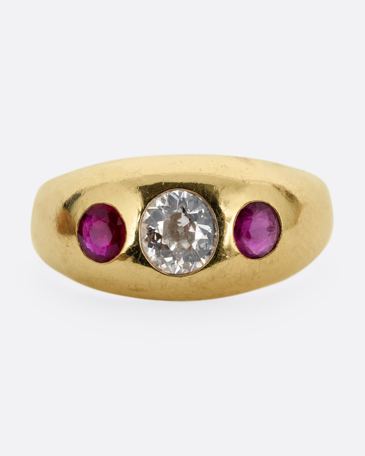 A yellow gold dome ring with a central diamond flanked by two rubies. Shown from the front.