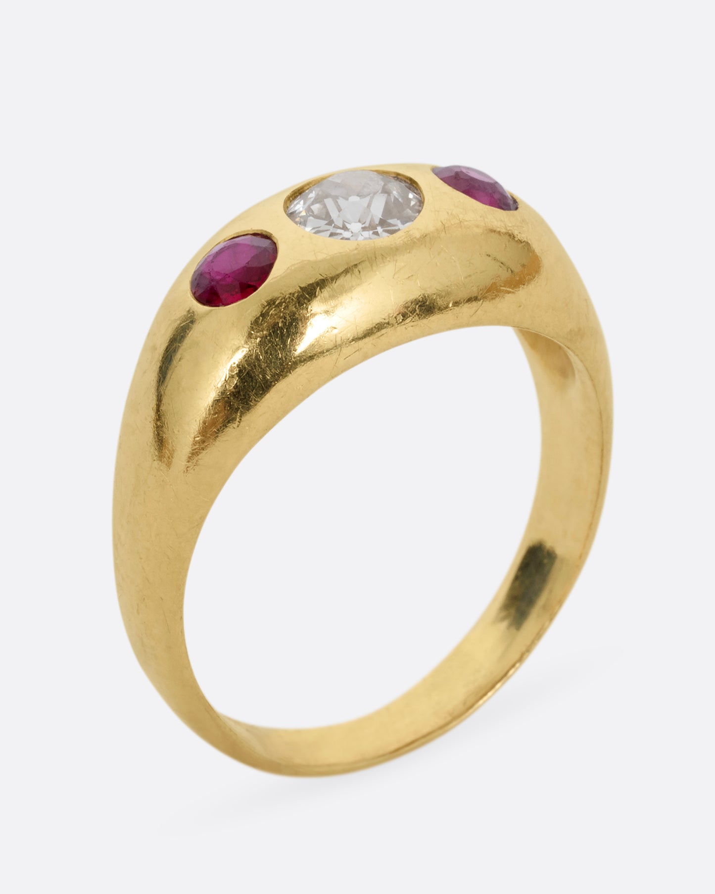 A yellow gold dome ring with a central diamond flanked by two rubies. Shown standing up from the side.