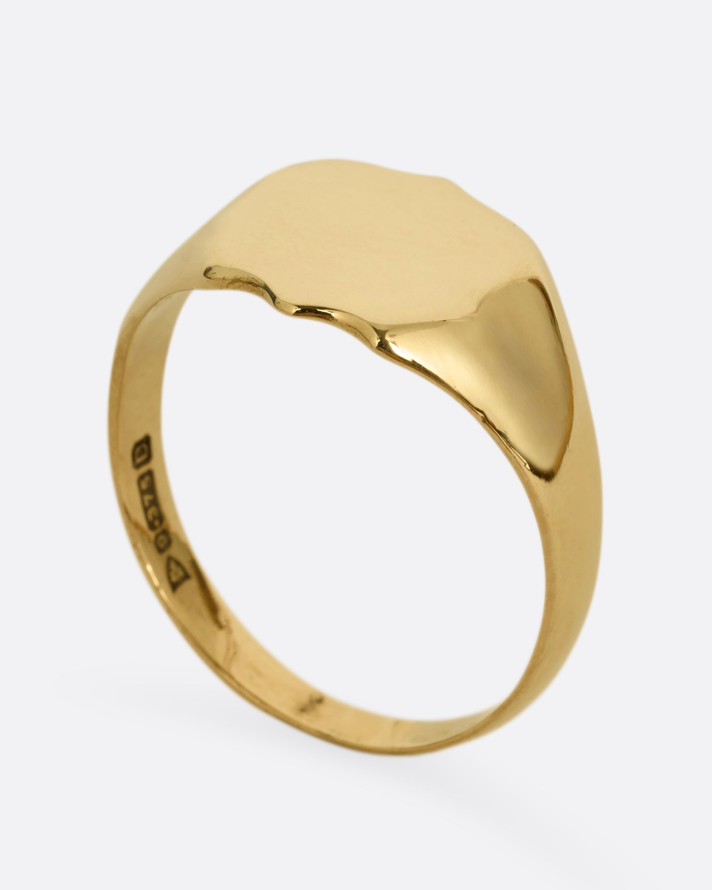 A yellow gold shield shaped signet ring. Shown standing up from the side.