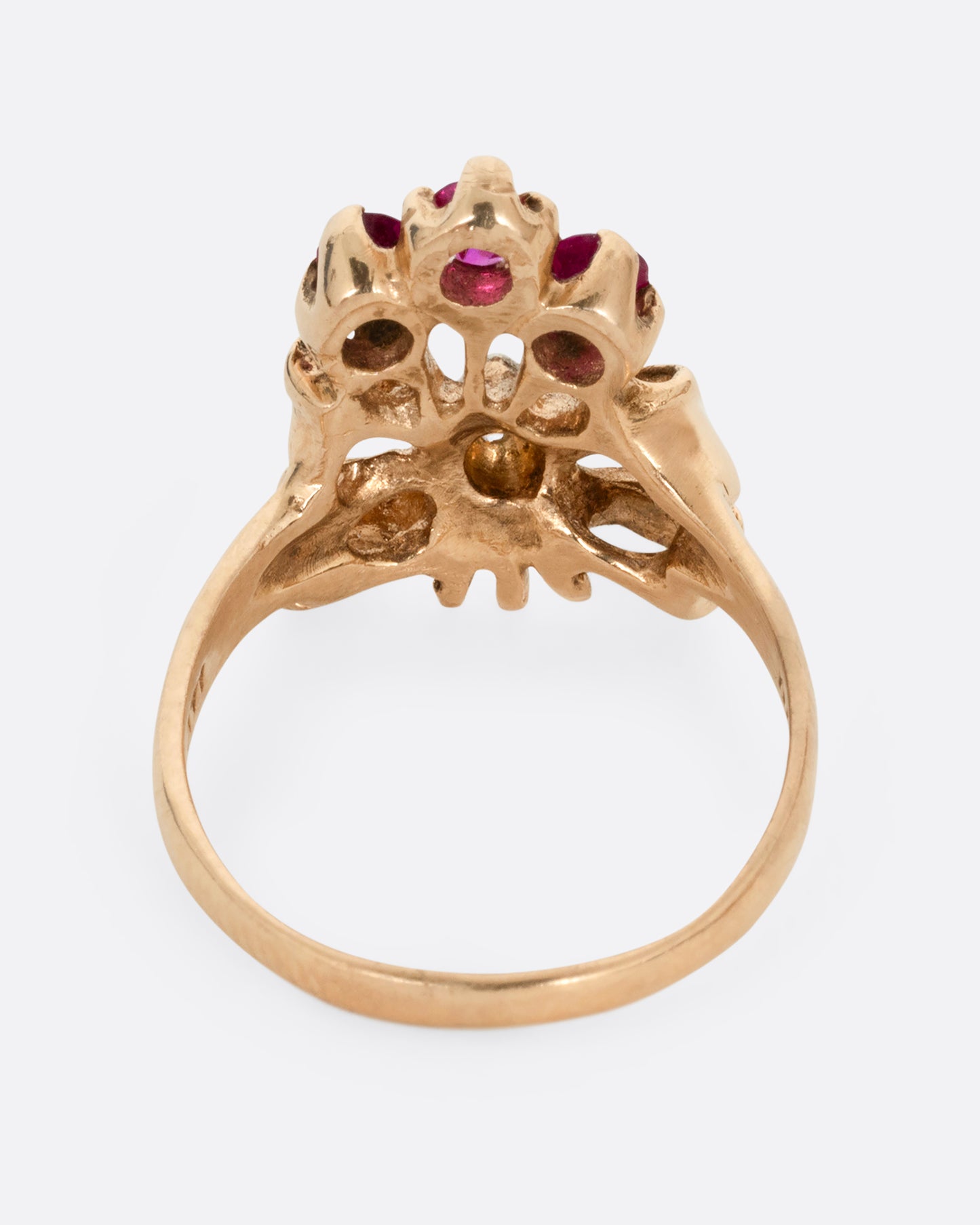 A yellow gold ring with a bouquet of ruby topped stems tied in a ribbon-like gold band and topped with a princess cut diamond. Shown from the back.