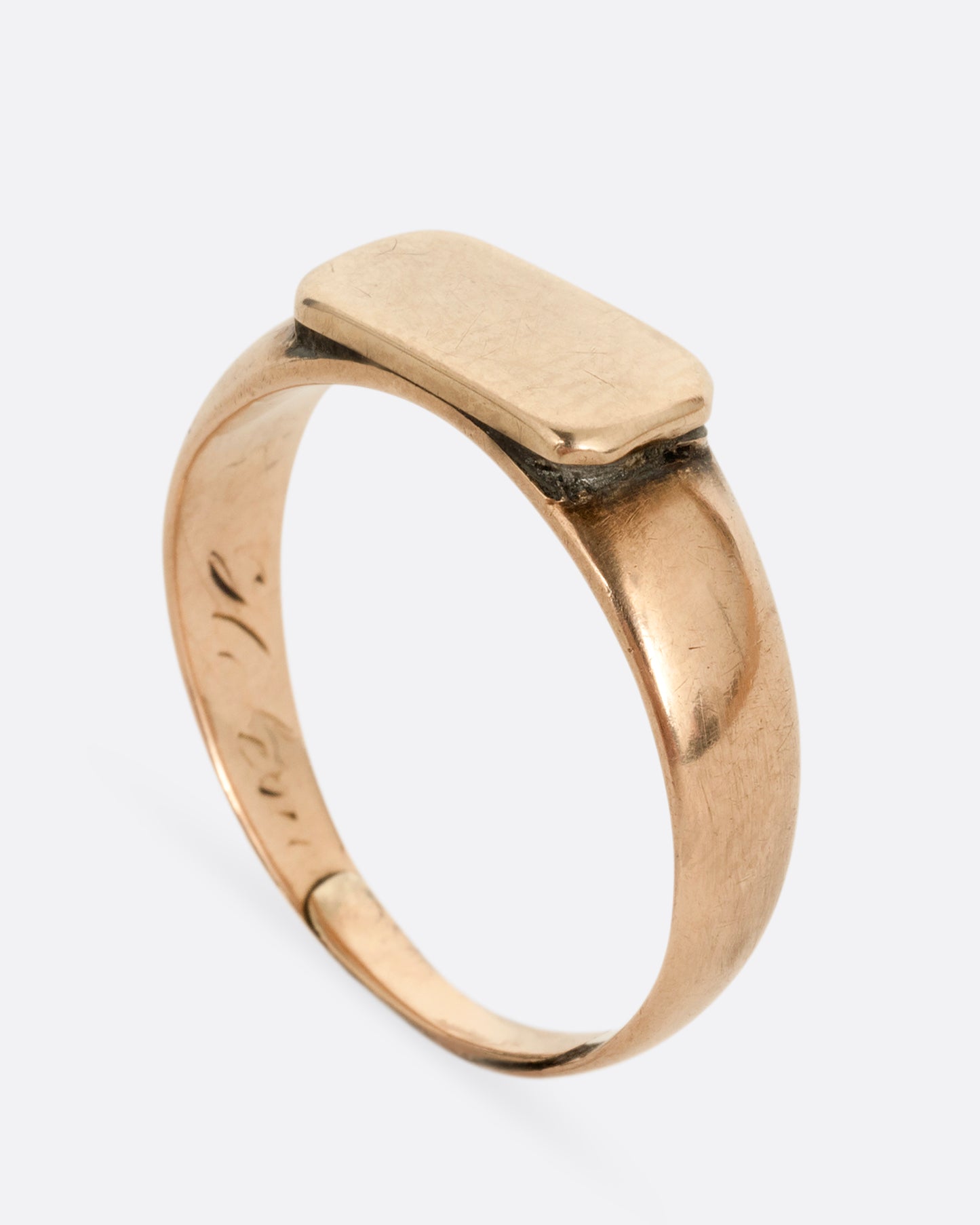 A yellow gold signet ring with a rectangular face. Shown standing up from the side.