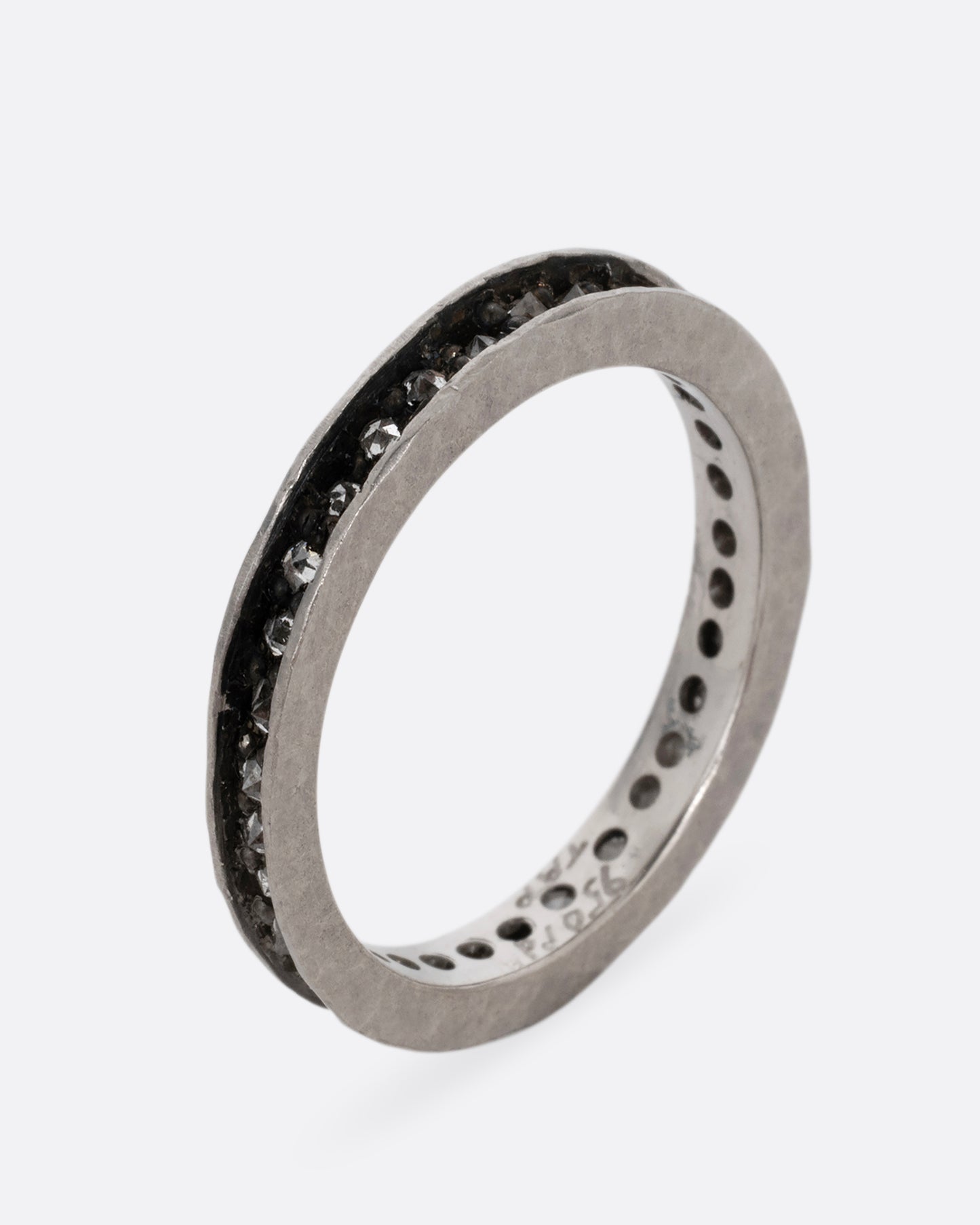 A palladium ring with a queue of diamonds set in a darkened center channel. Shown standing up from the side.