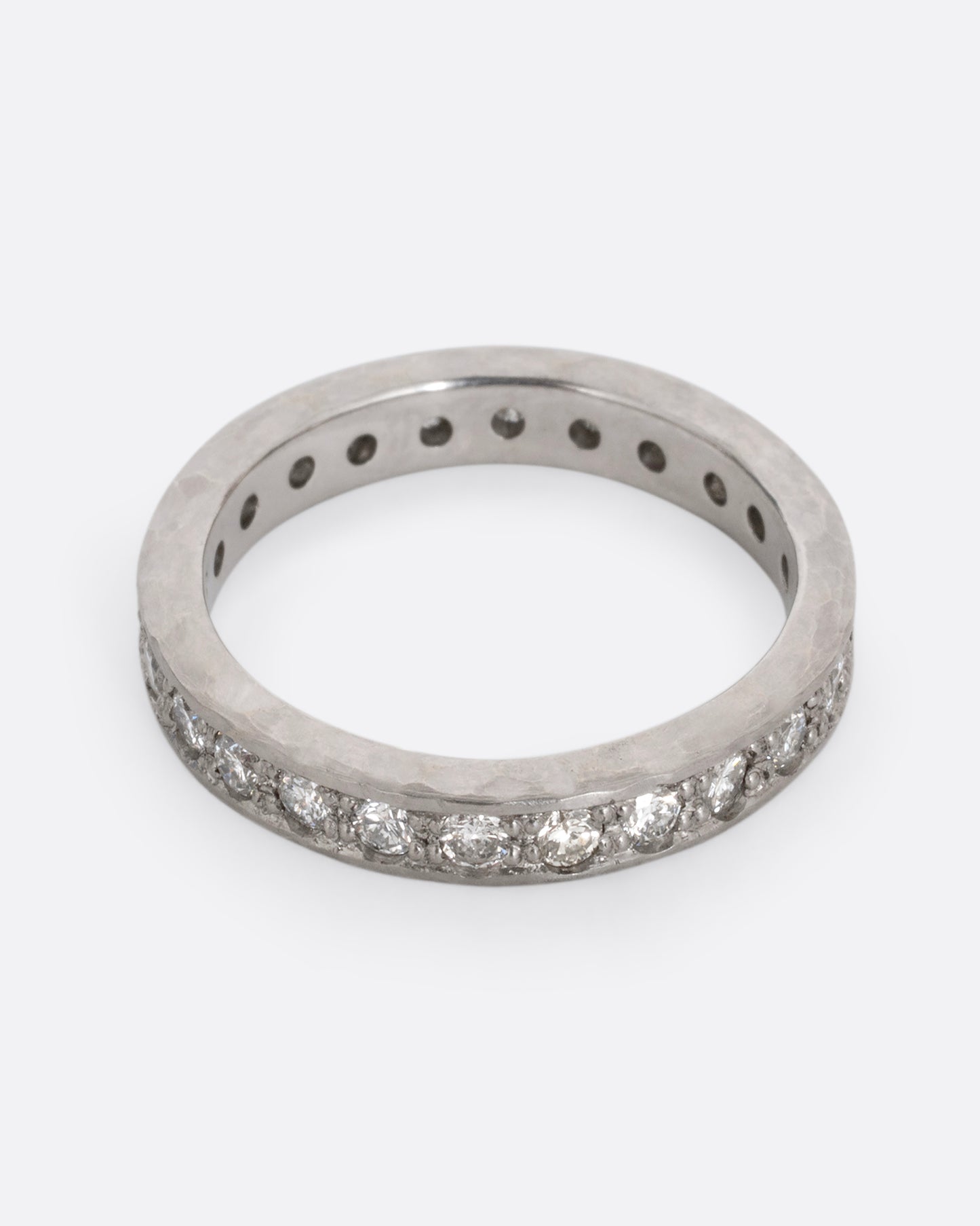 A platinum band with hammered edges and a darkened center with diamonds throughout. Shown from the front.
