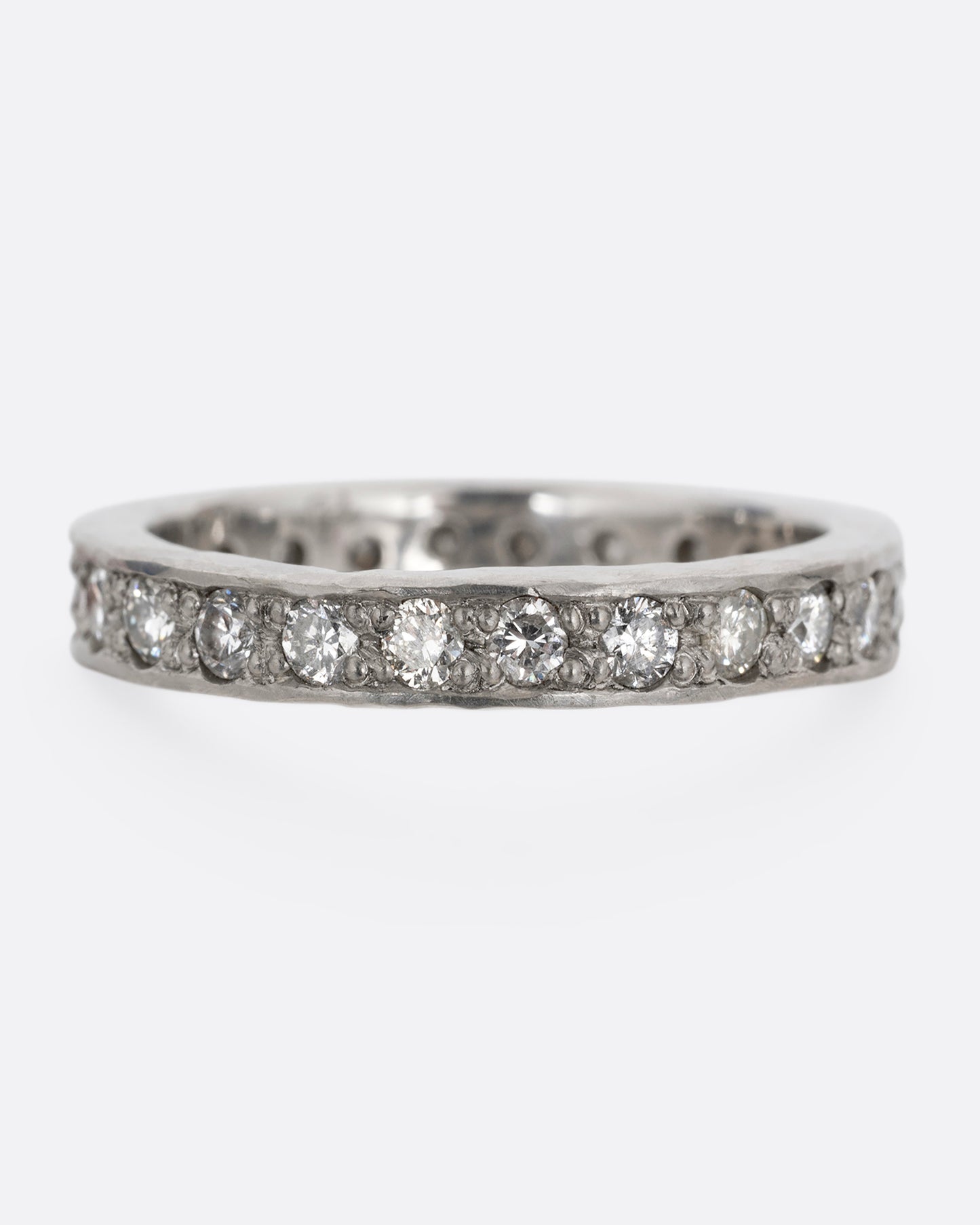 A platinum band with hammered edges and a darkened center with diamonds throughout. Shown from the front.