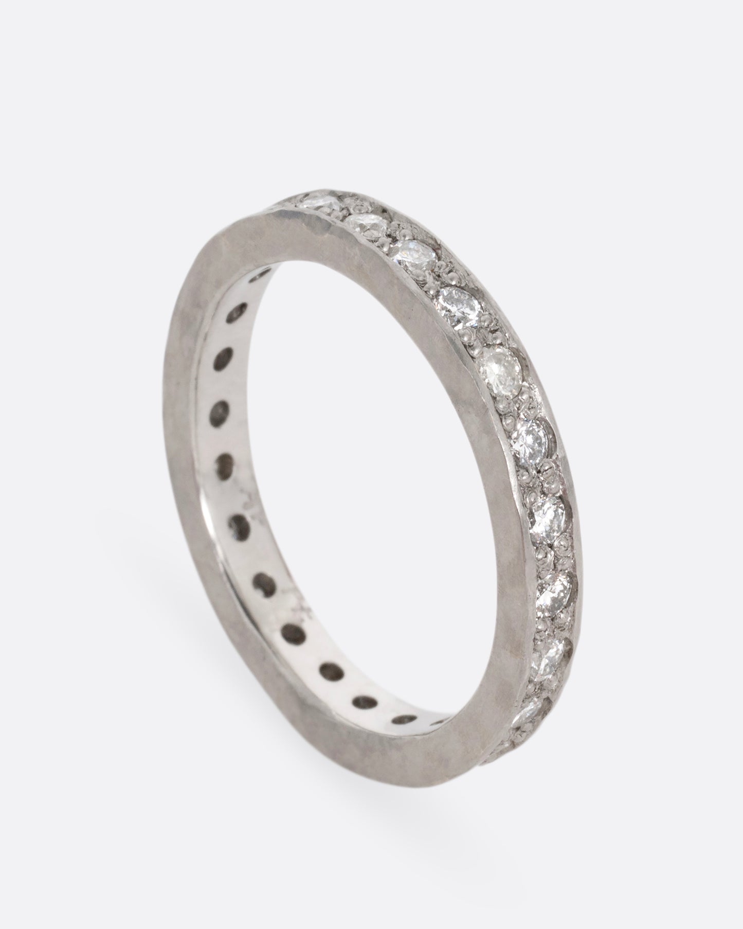 A platinum band with hammered edges and a darkened center with diamonds throughout. Shown standing up from the side.