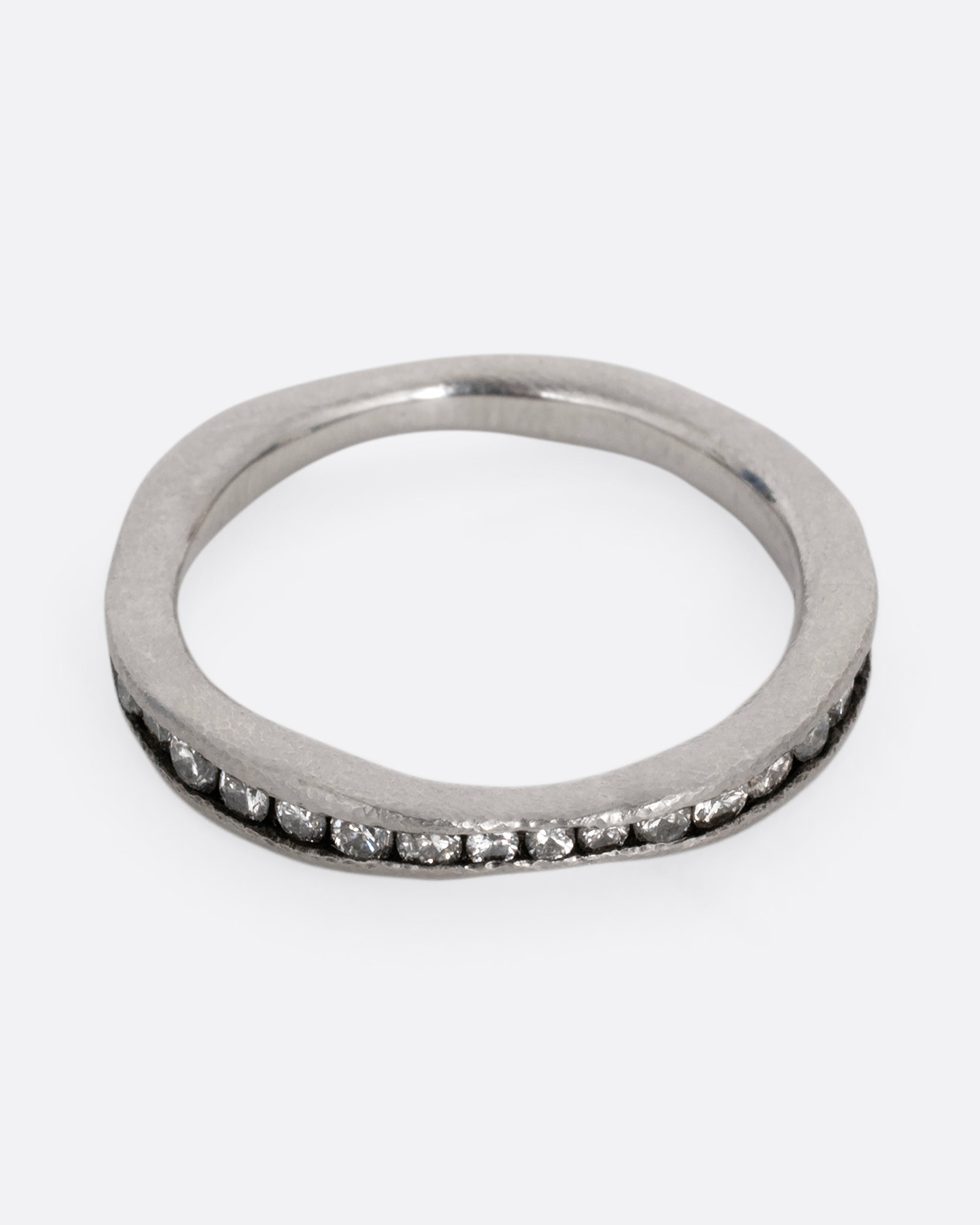 A nonuniform platinum ring with a darkened channel filled with diamonds. Shown from the front.