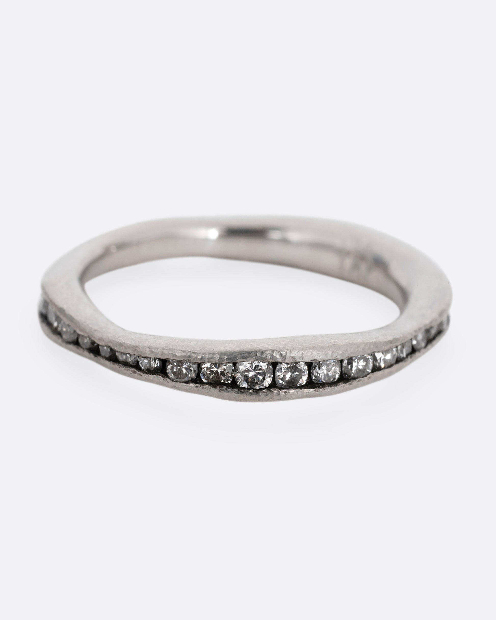 A nonuniform platinum ring with a darkened channel filled with diamonds. Shown from the front.