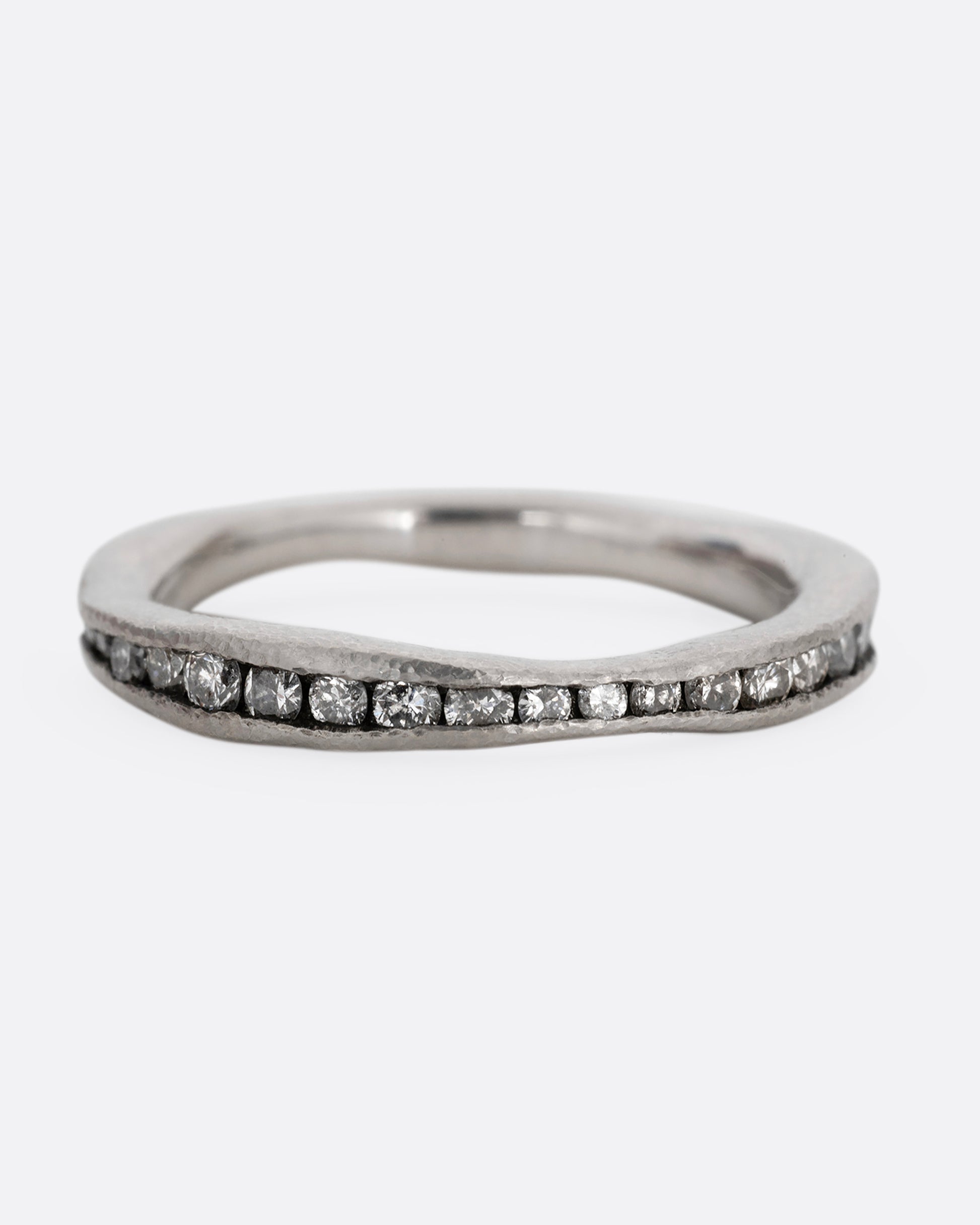 A nonuniform platinum ring with a darkened channel filled with diamonds. Shown from the front.