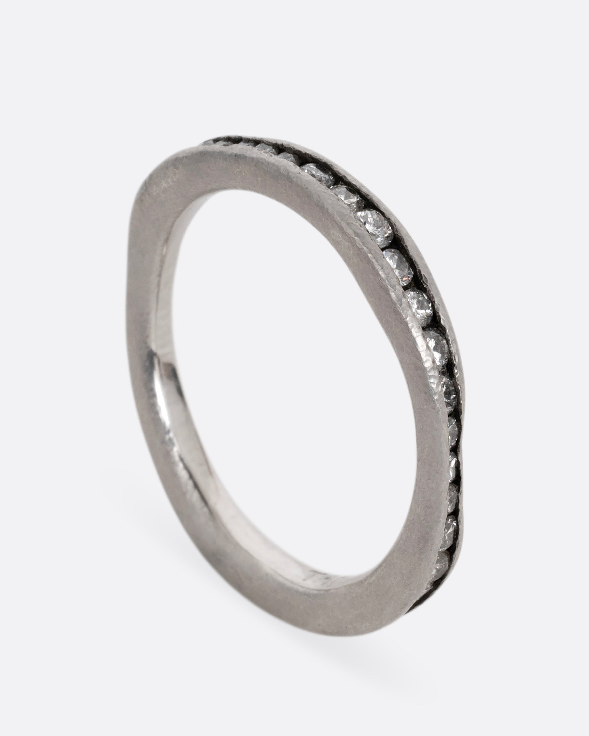 A nonuniform platinum ring with a darkened channel filled with diamonds. Shown standing up from the side.