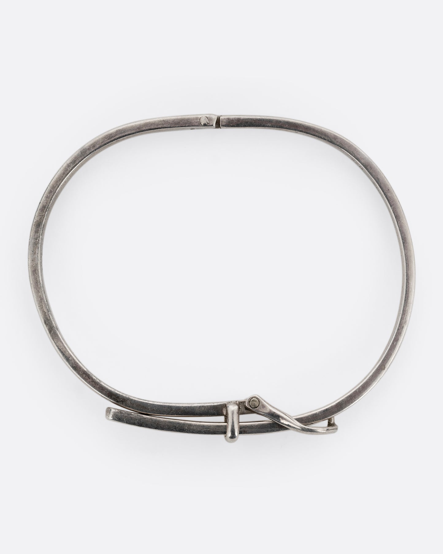 A narrow silver hinged bracelet with a buckle front. Shown from the top.