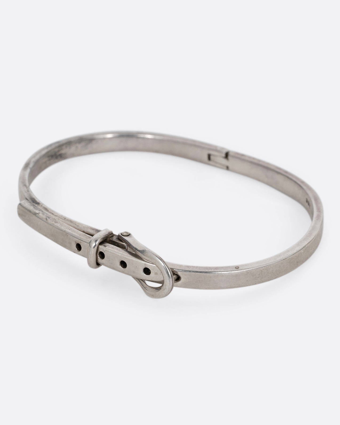 A narrow silver hinged bracelet with a buckle front. Shown from the side.