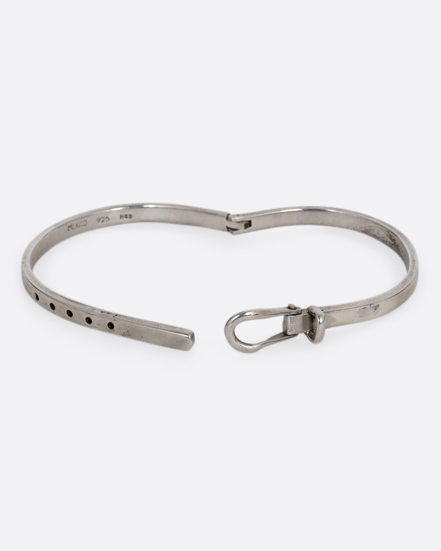 A narrow silver hinged bracelet with a buckle front. Shown open from the front.