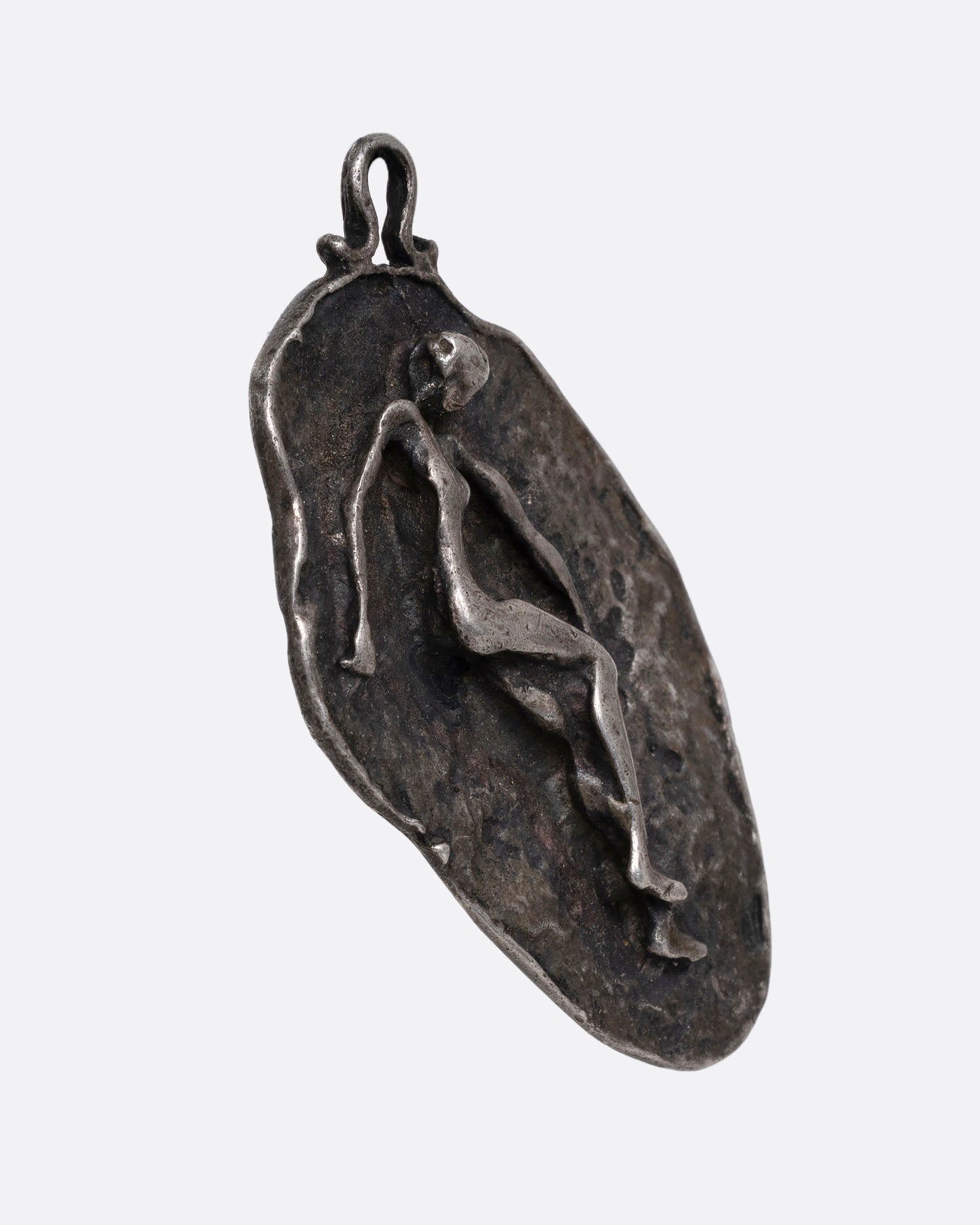 A silver freeform pendant with a figure emerging from a textural background. Shown from the side.