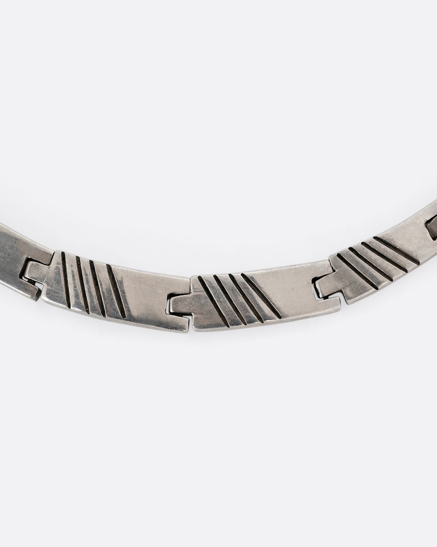 A silver collar necklace with hinged rectangular links and striped etchings. Shown close up.