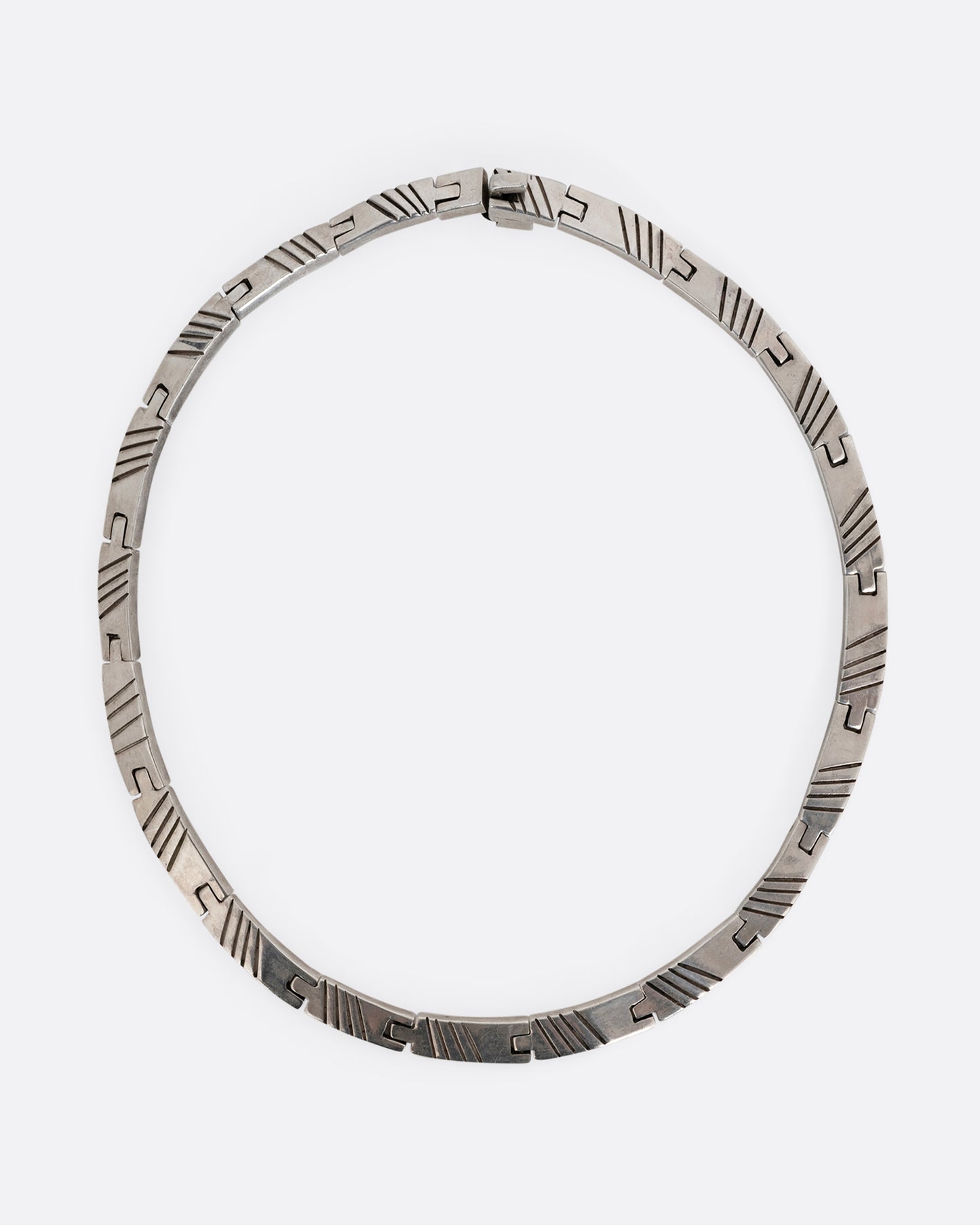 A silver collar necklace with hinged rectangular links and striped etchings. Shown from the top.
