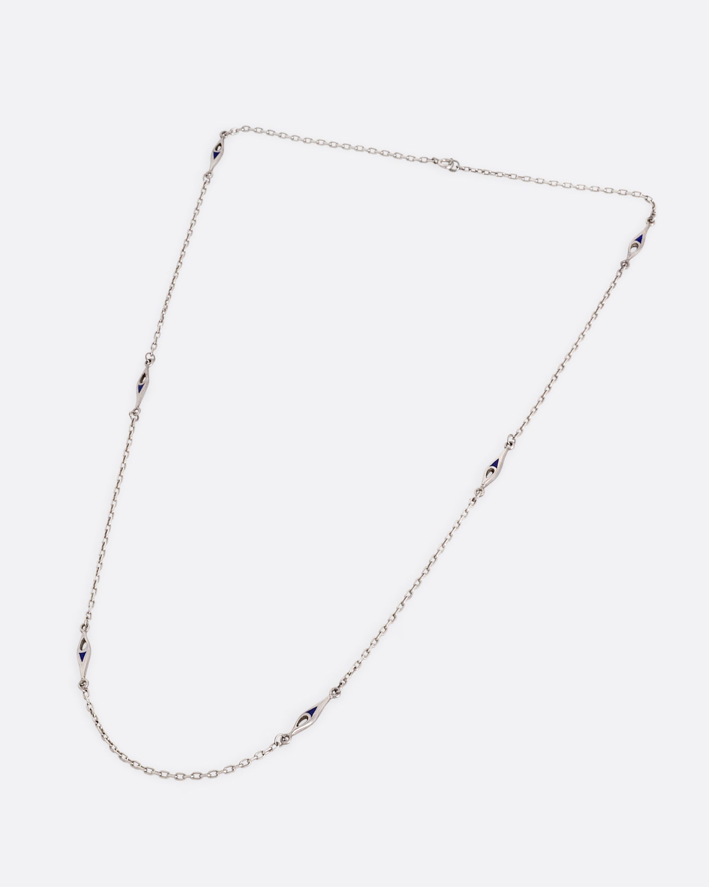 A silver cable chain necklace with marquise shaped stations of blue enamel. Shown from the front.