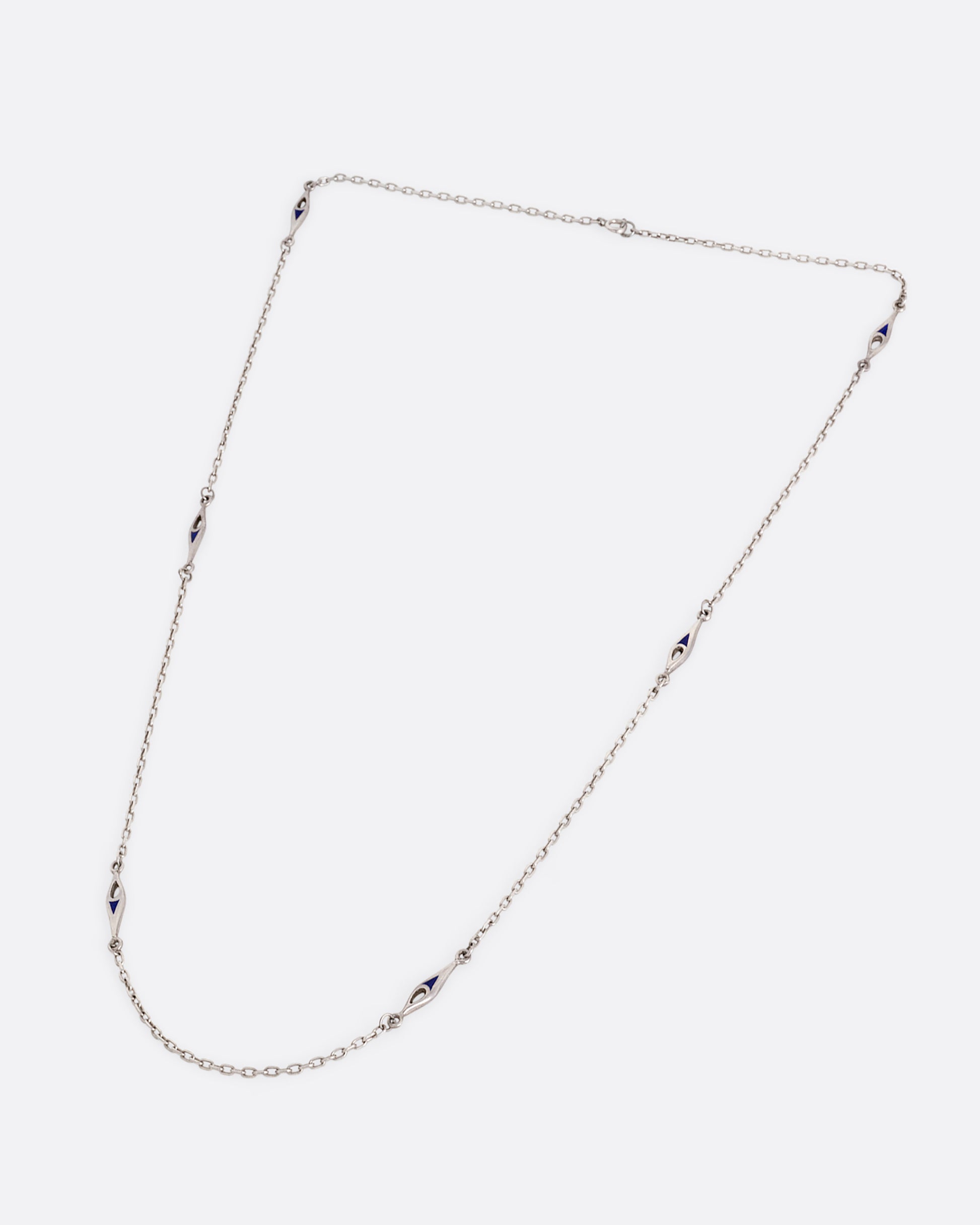 A silver cable chain necklace with marquise shaped stations of blue enamel. Shown from the front.