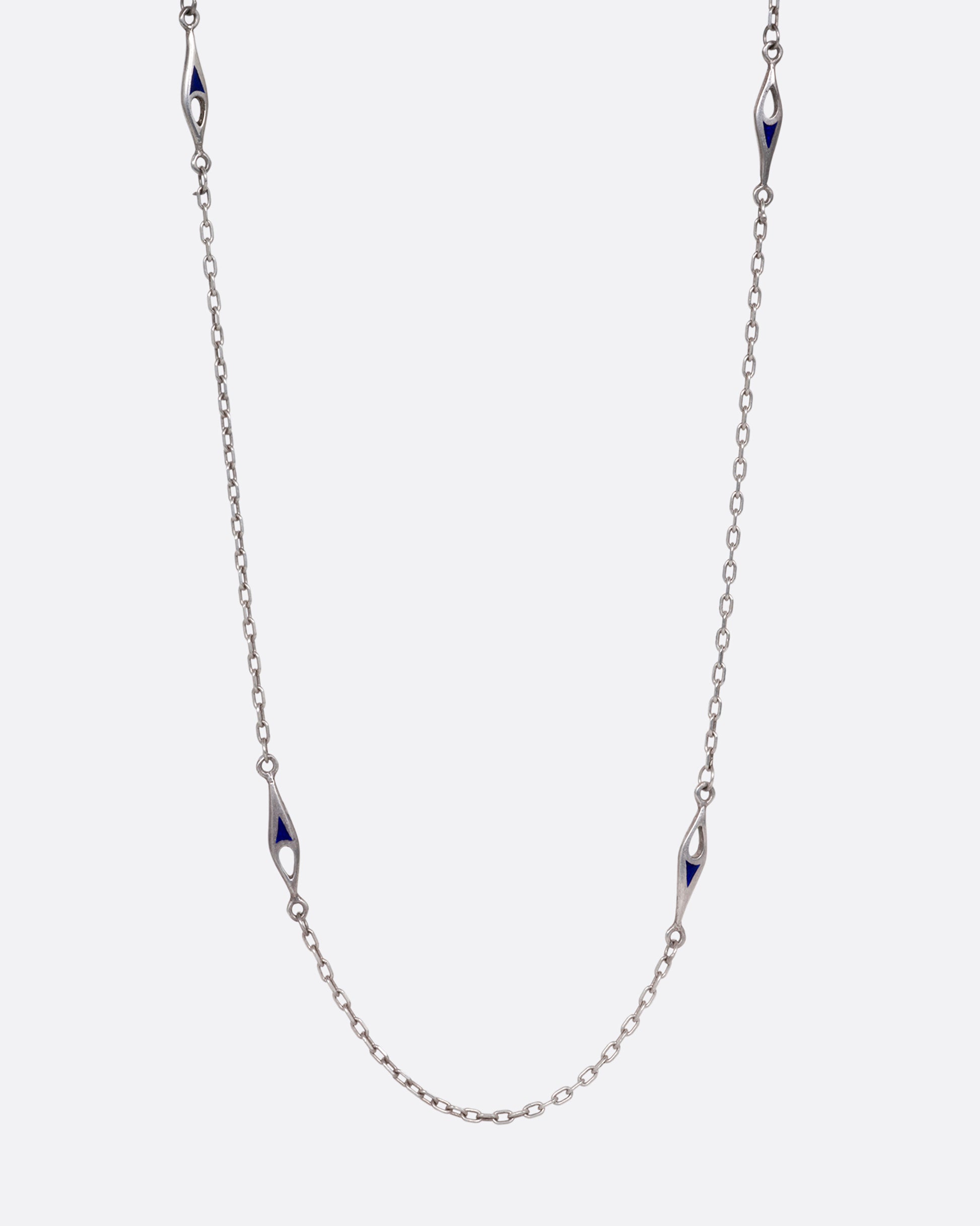 A silver cable chain necklace with marquise shaped stations of blue enamel. Shown from the front.