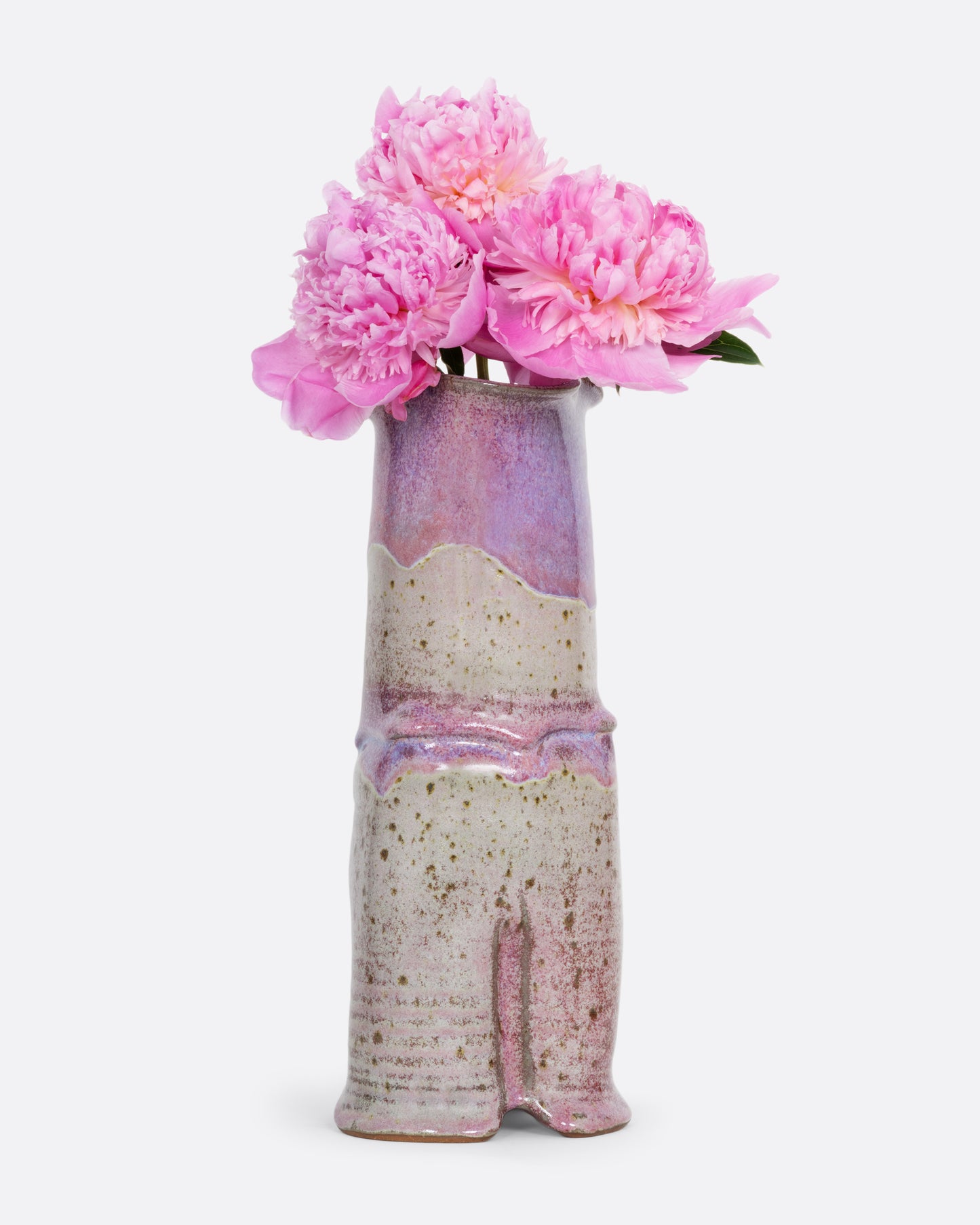 A tall ceramic vase with a tiered silhouette, fluted top, and gray and lavender color scheme. Shown from the front with pink peonies in it.