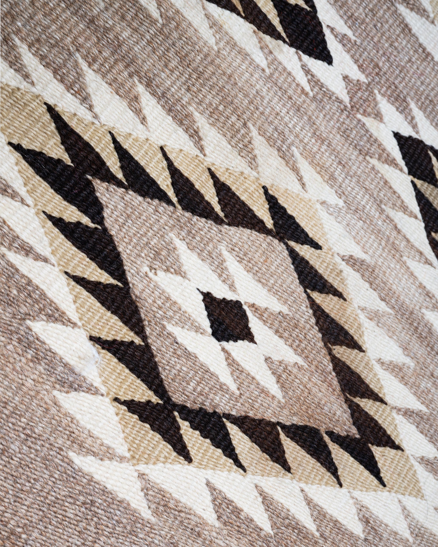 A close up of a tan, black, and white Navajo Diamond Eye Dazzler rug with a serrated diamond motif.