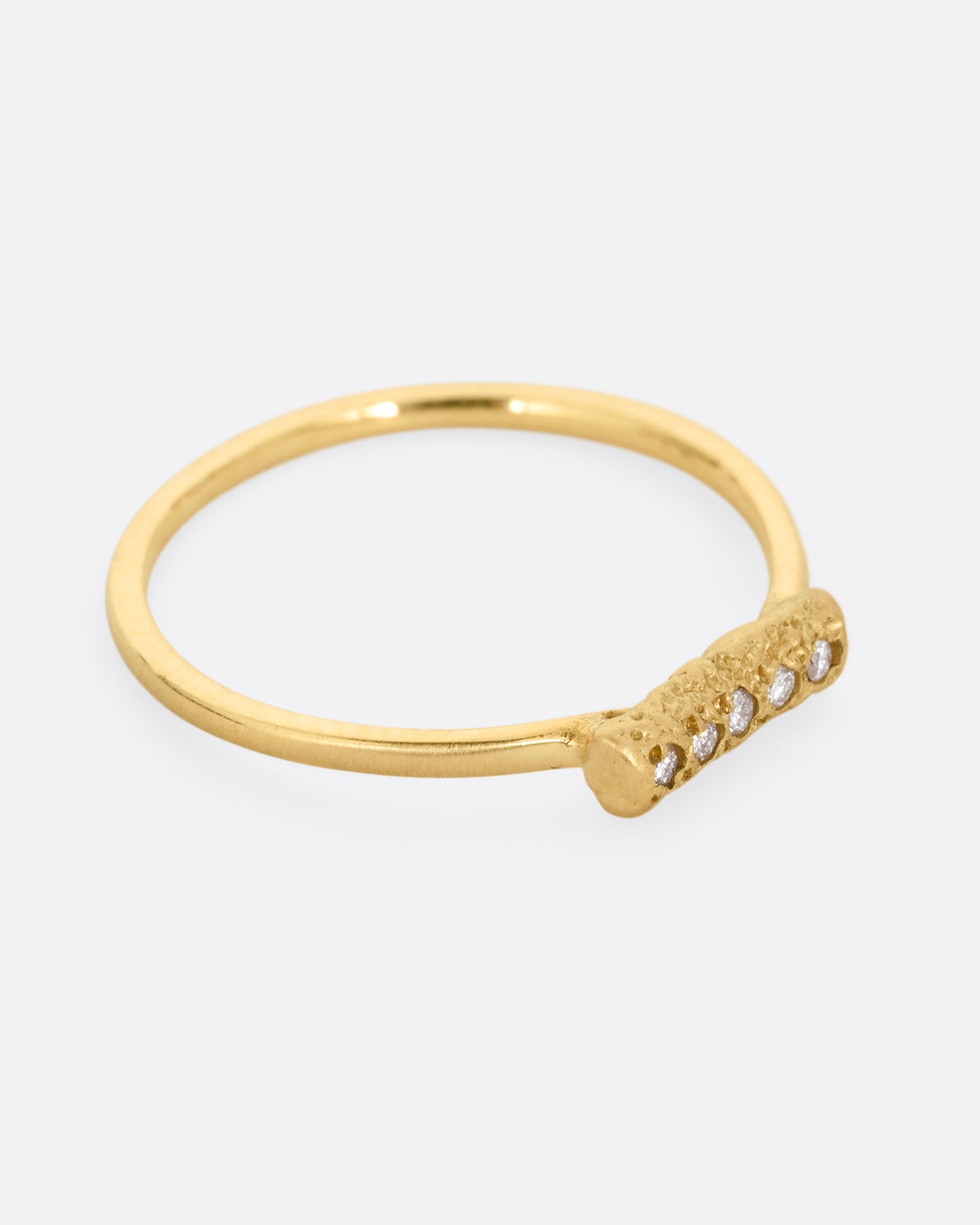 A yellow gold ring with five diamonds set on a textured face. Shown from the side.
