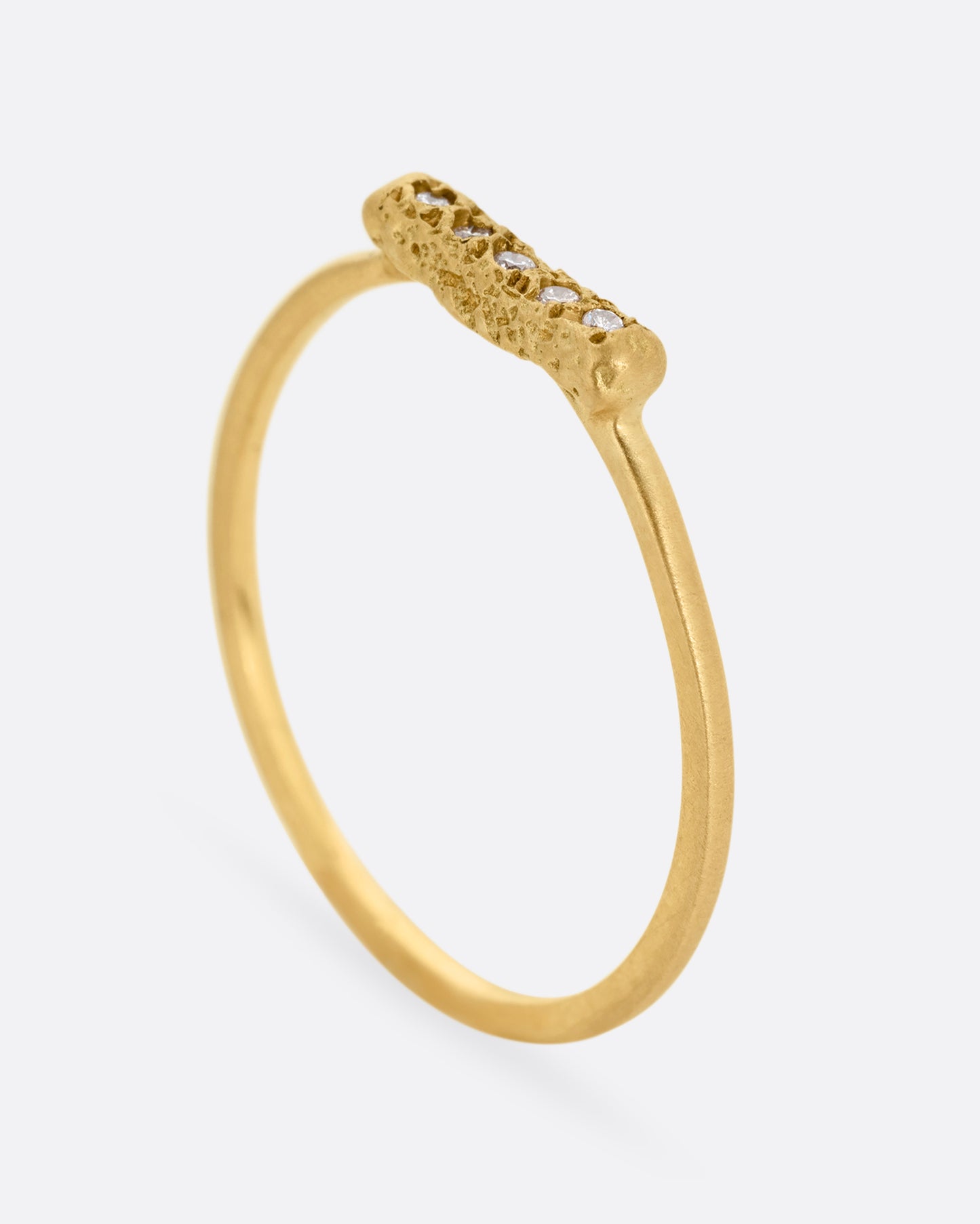 A yellow gold ring with five diamonds set on a textured face. Shown standing up from the side.