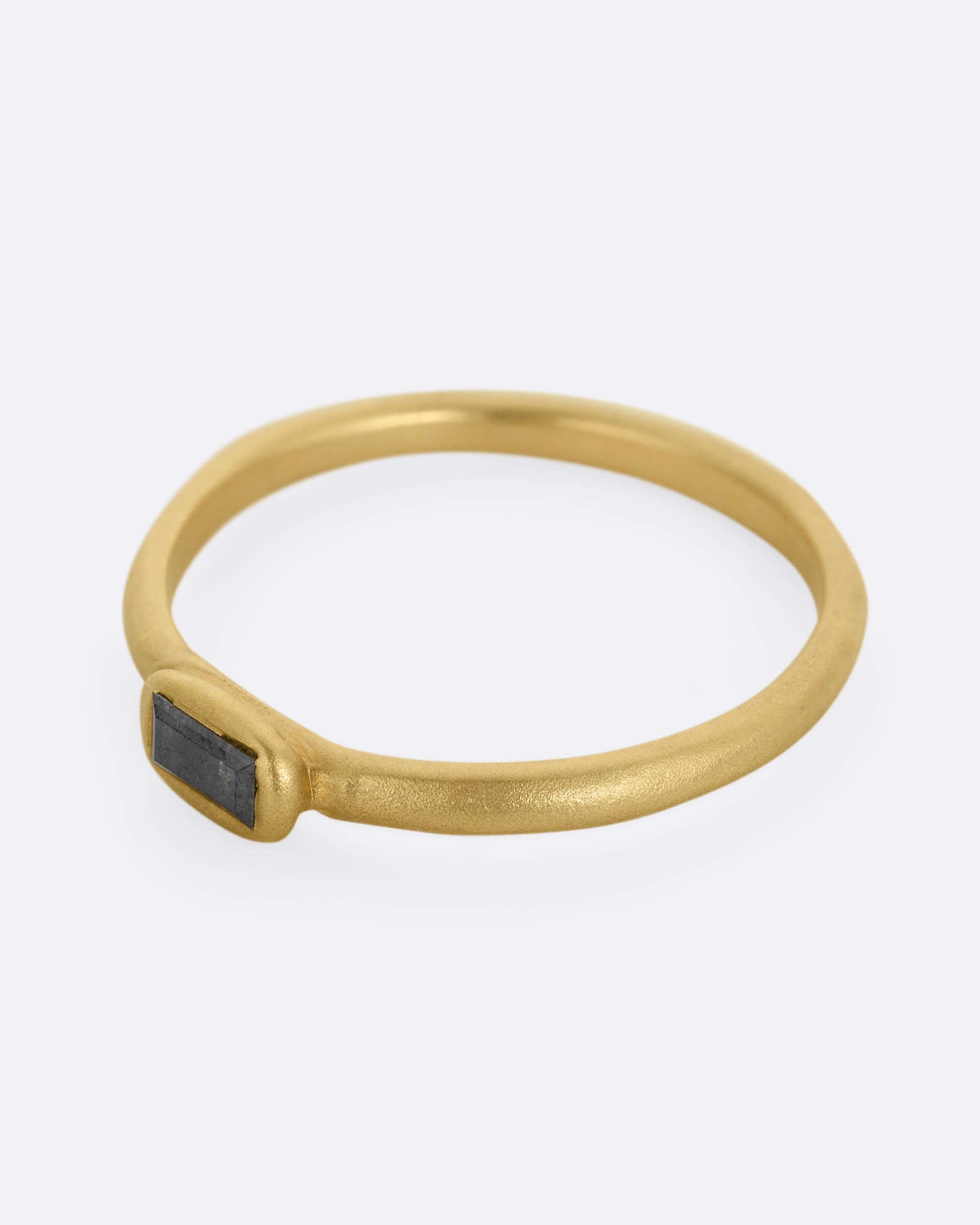 A yellow gold ring with a horizontally set salt and pepper baguette diamond, shown from the side.