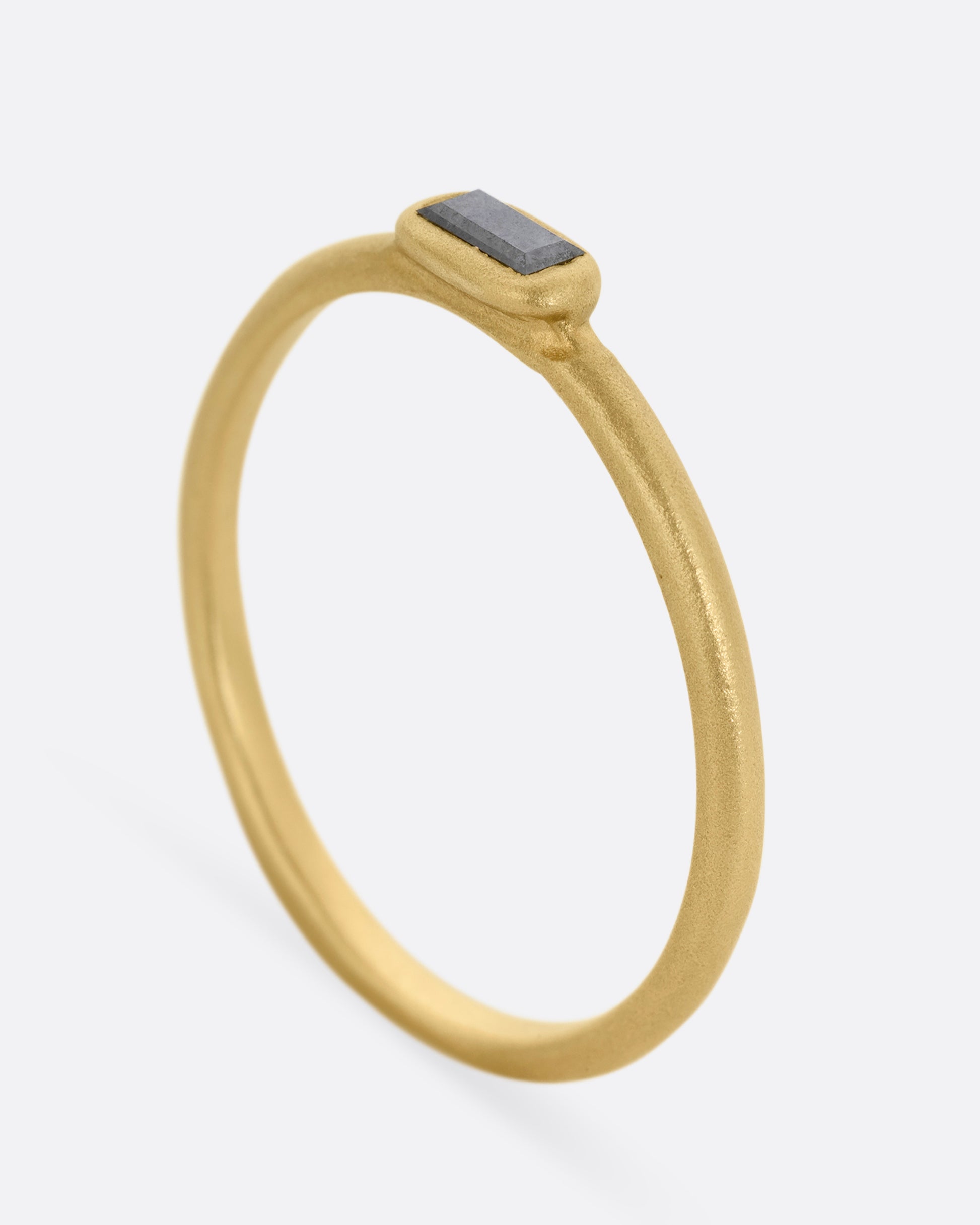 A yellow gold ring with a horizontally set salt and pepper baguette diamond, shown standing up from the side.