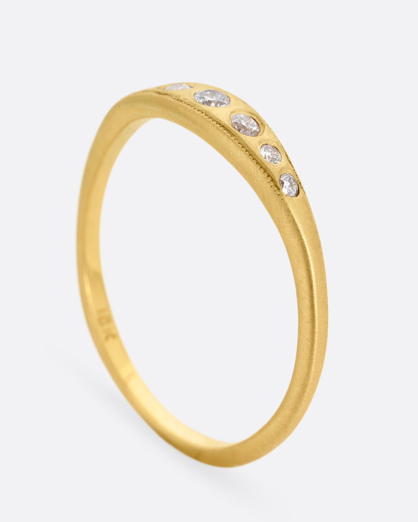 A yellow gold ring with seven diamonds. Shown standing up from the side.