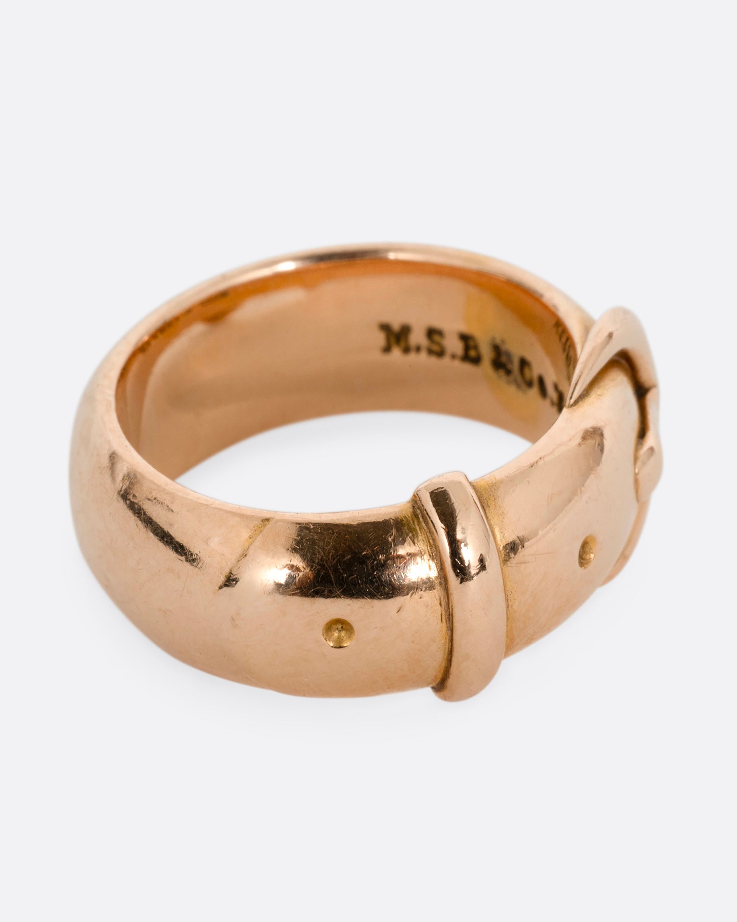 A yellow gold belt buckle ring with a curved edge. Shown from the side.