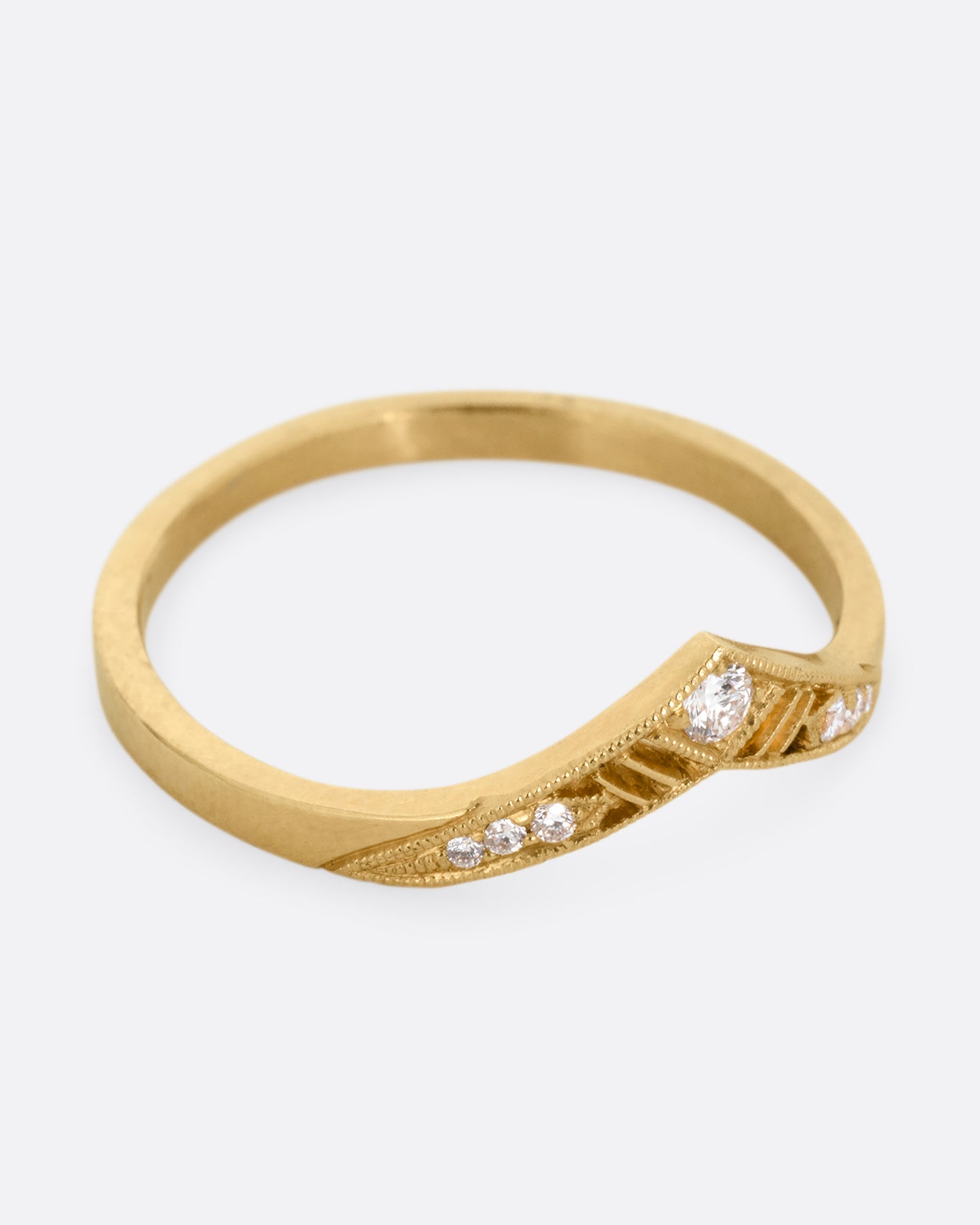 A slightly pointed yellow gold ring with diamonds and cutouts shown from the from the side.